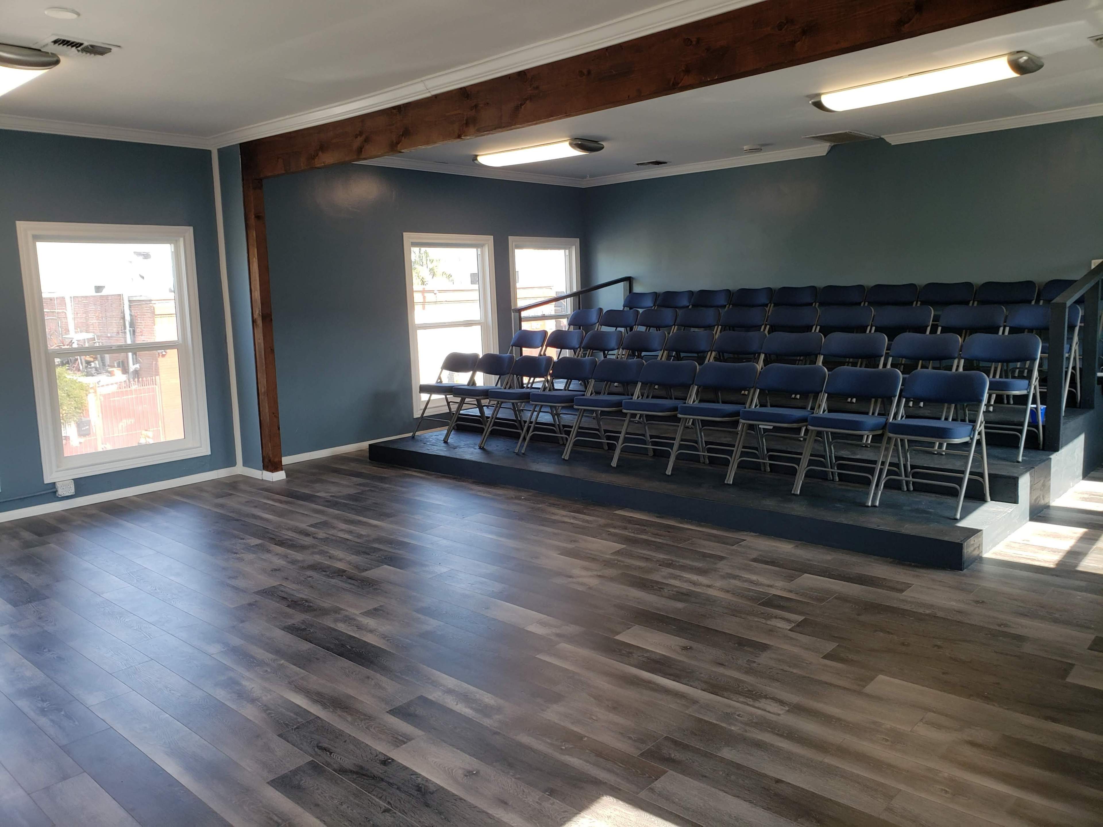 A spacious room with blue walls, a wooden beam, and rows of metal folding chairs on a raised platform.