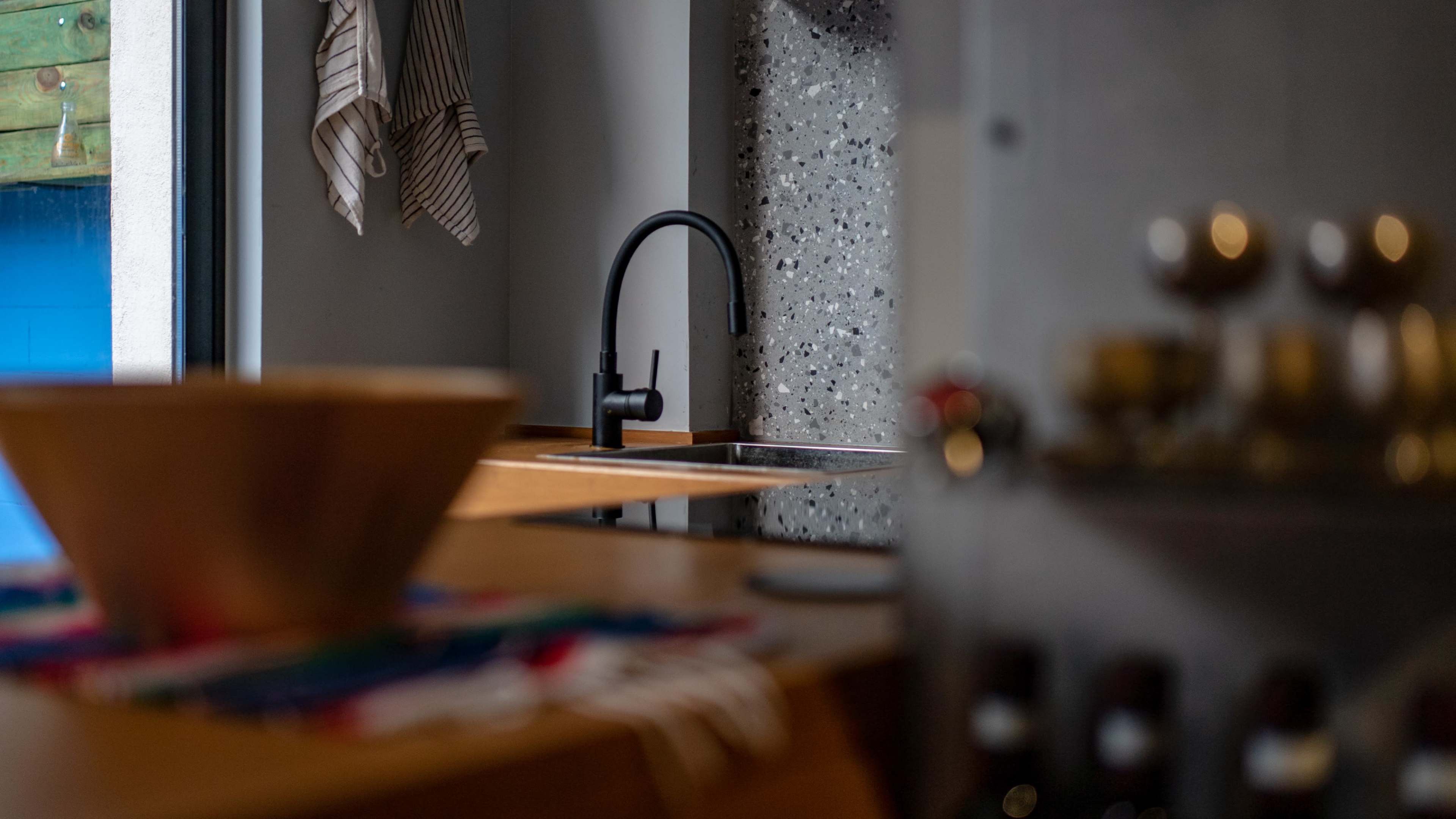 A modern kitchen with a wooden bowl on a countertop, a sleek black faucet, and textured grey wall accents.