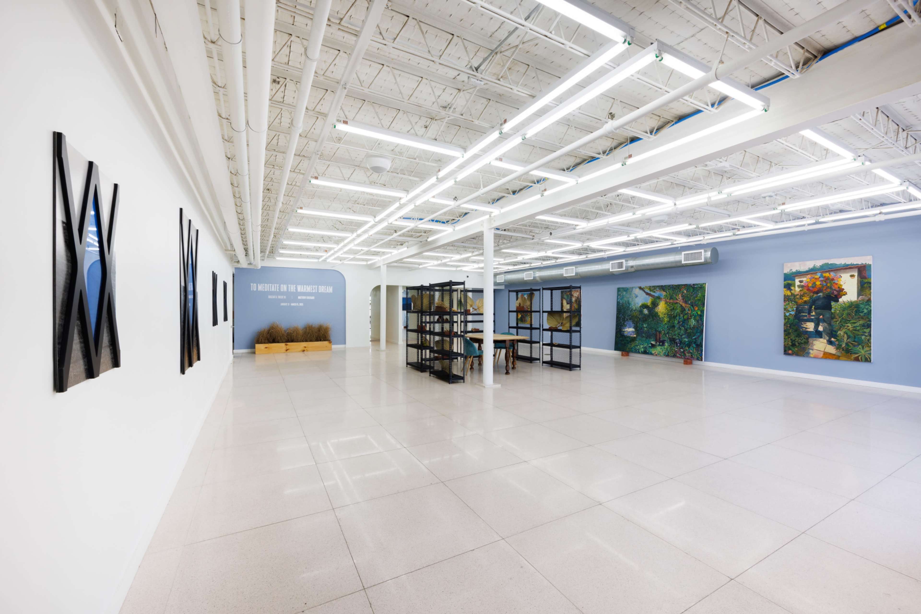 The image shows a spacious art gallery featuring two large art pieces on the walls, a central display shelf, and a light-colored tiled floor.