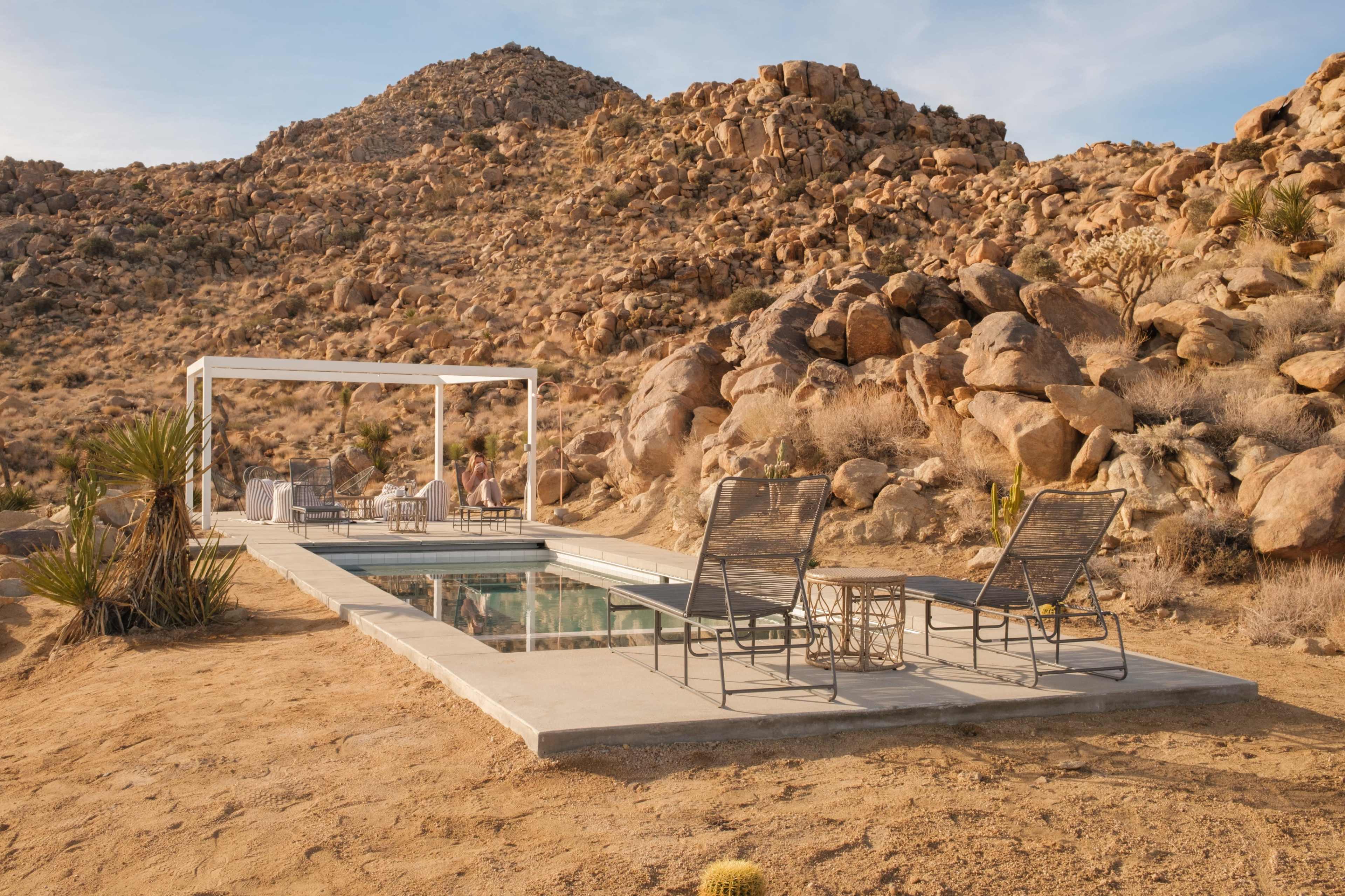 A modern pool area with lounge chairs is situated against a backdrop of rugged rocks and desert terrain.