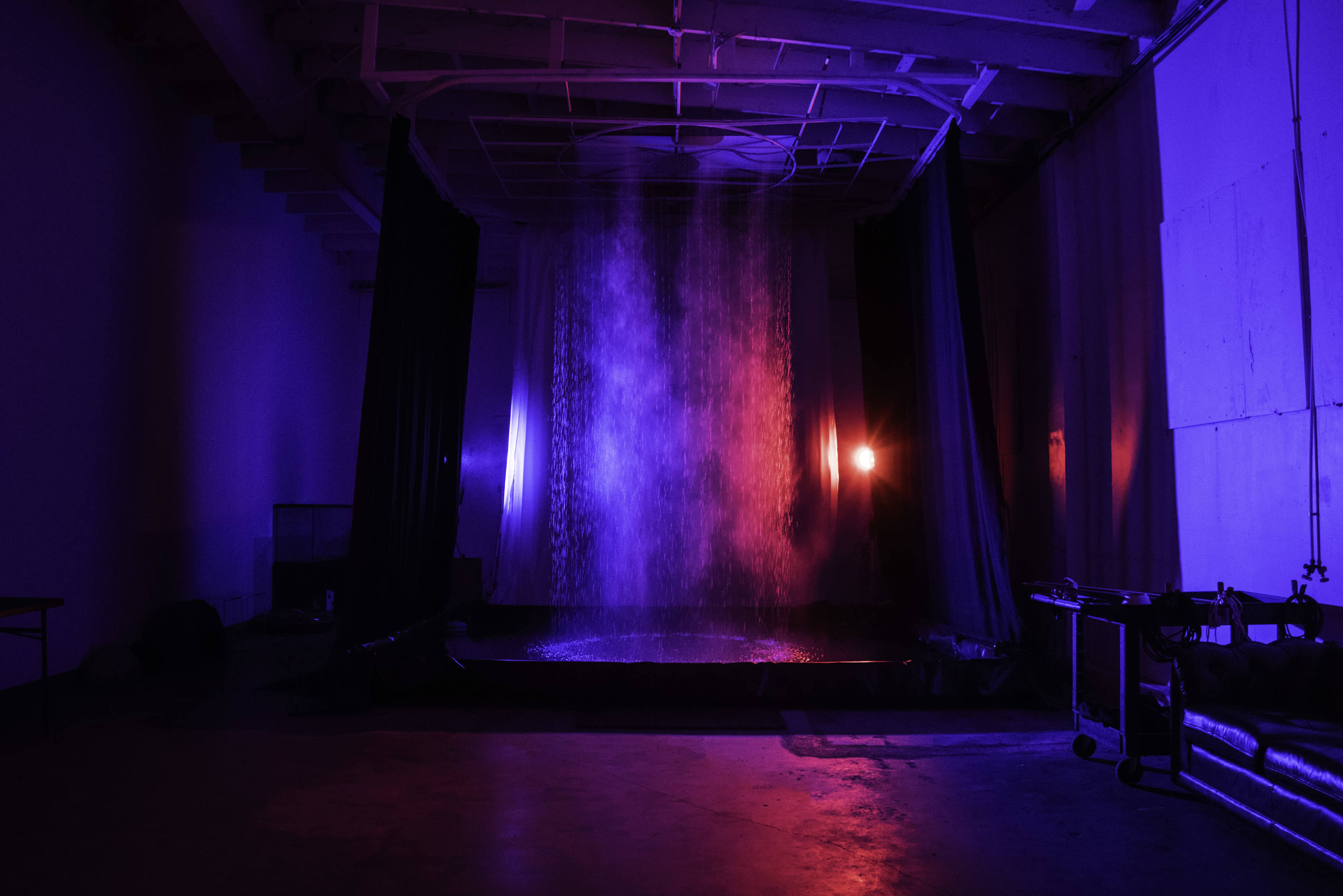 A water feature cascades down in a dimly lit room, illuminated by contrasting blue and red lights.