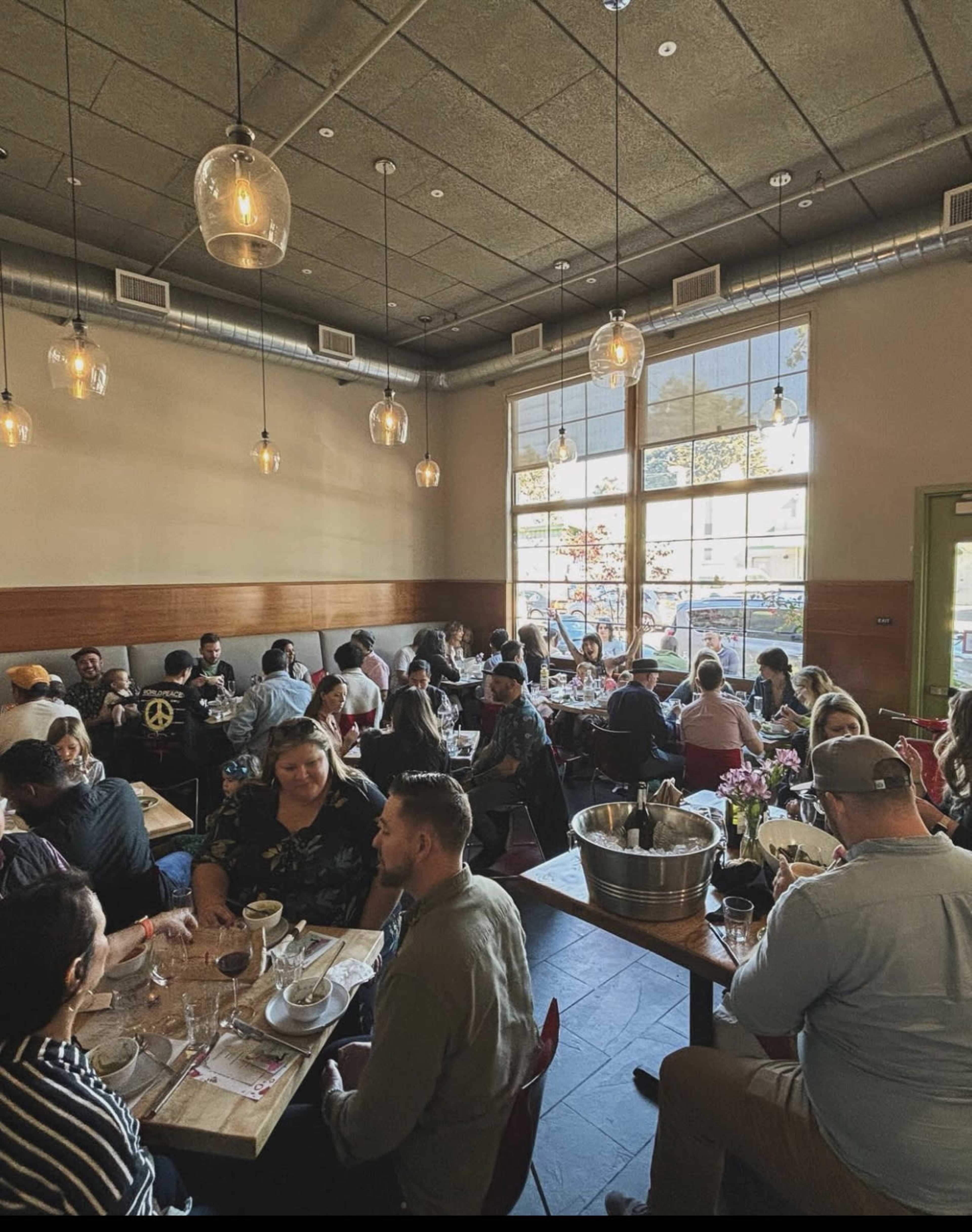 A bustling restaurant filled with groups of people dining at tables under pendant lights.