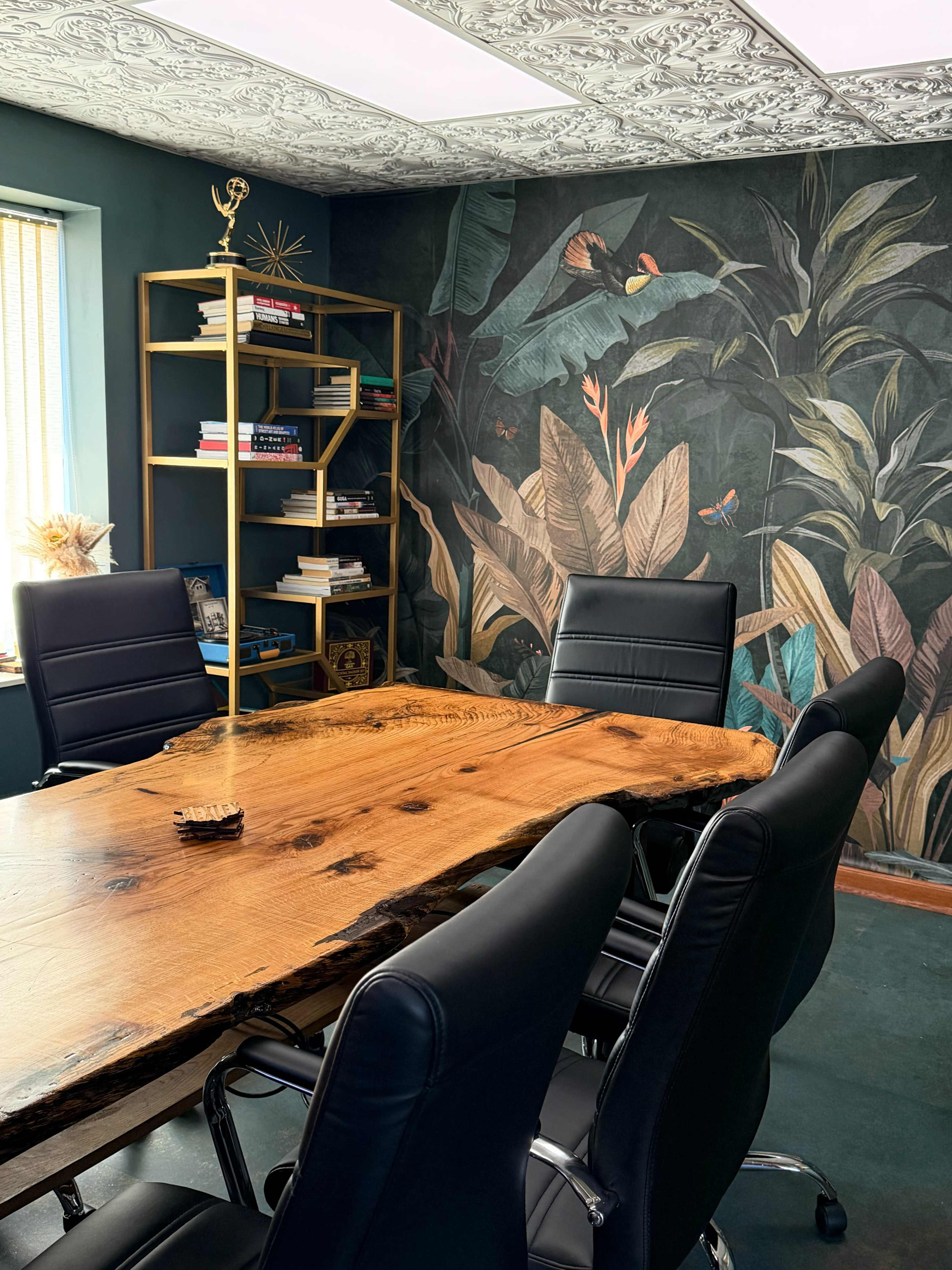 The image shows a conference room with a large wooden table, black leather chairs, and a wall decorated with tropical plants and butterflies.