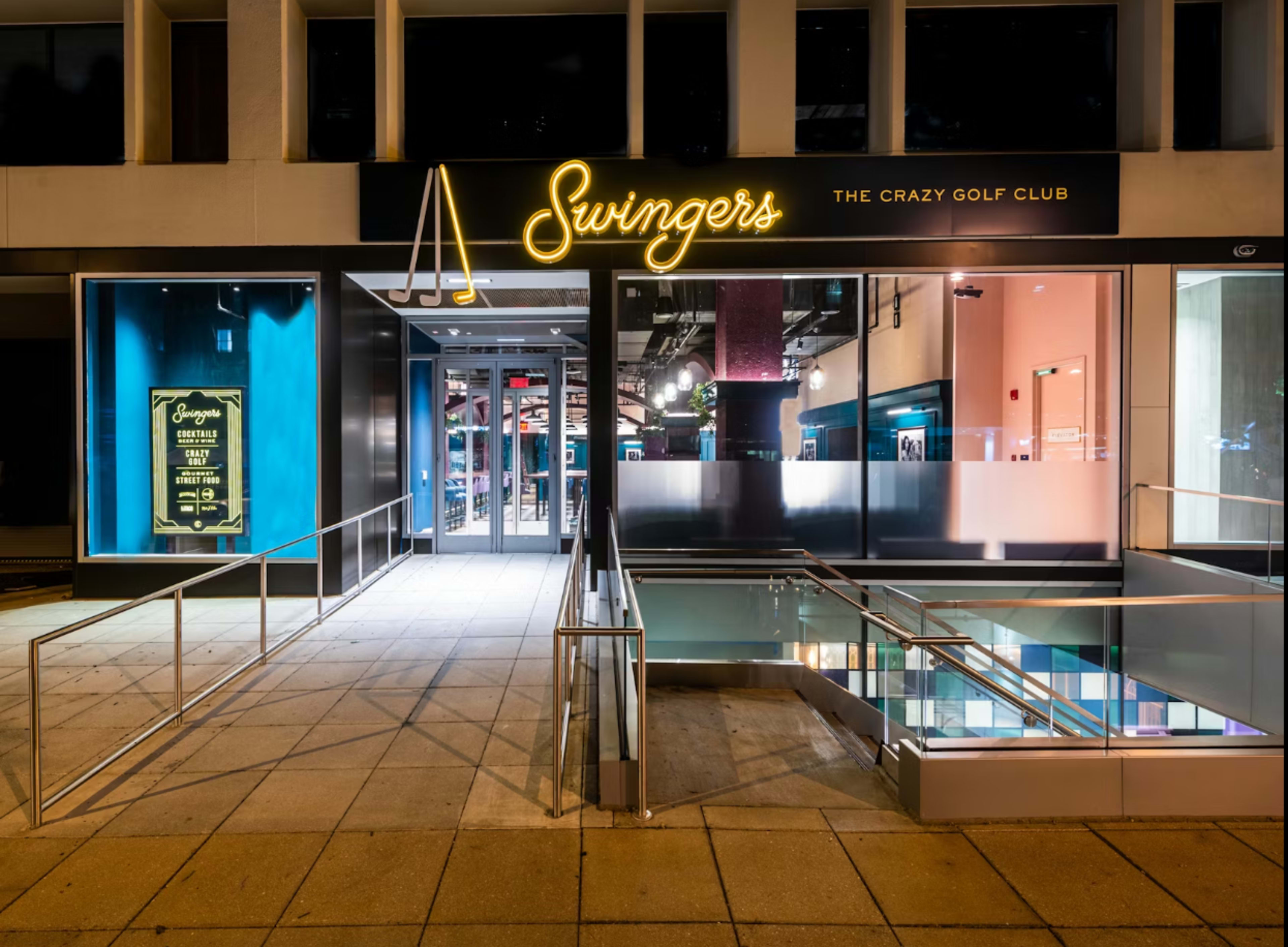 The image shows the entrance of a venue called "Swingers: The Crazy Golf Club," featuring illuminated signage and a glass staircase.