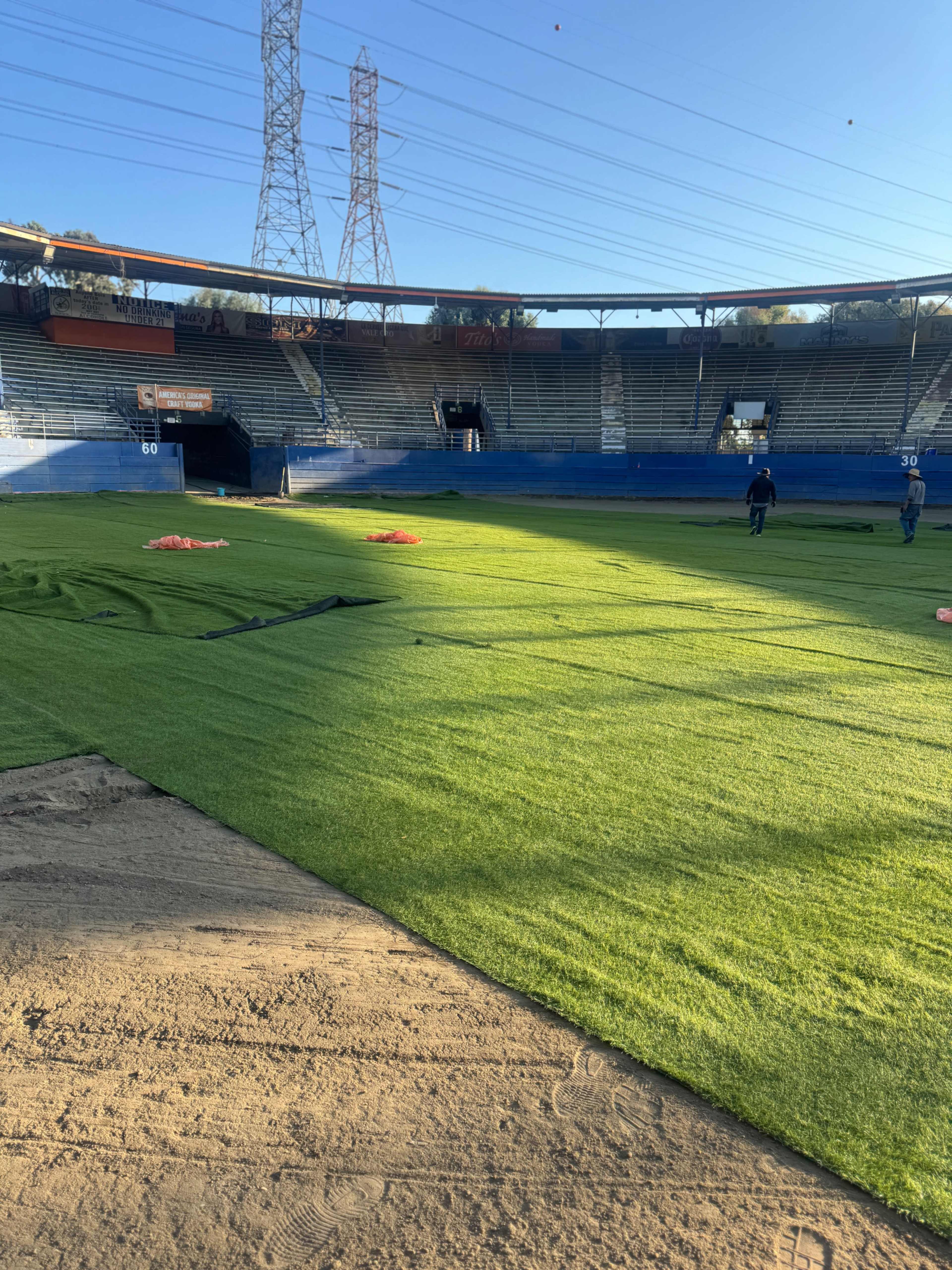 Workers are installing artificial grass on a baseball field in a stadium setting.