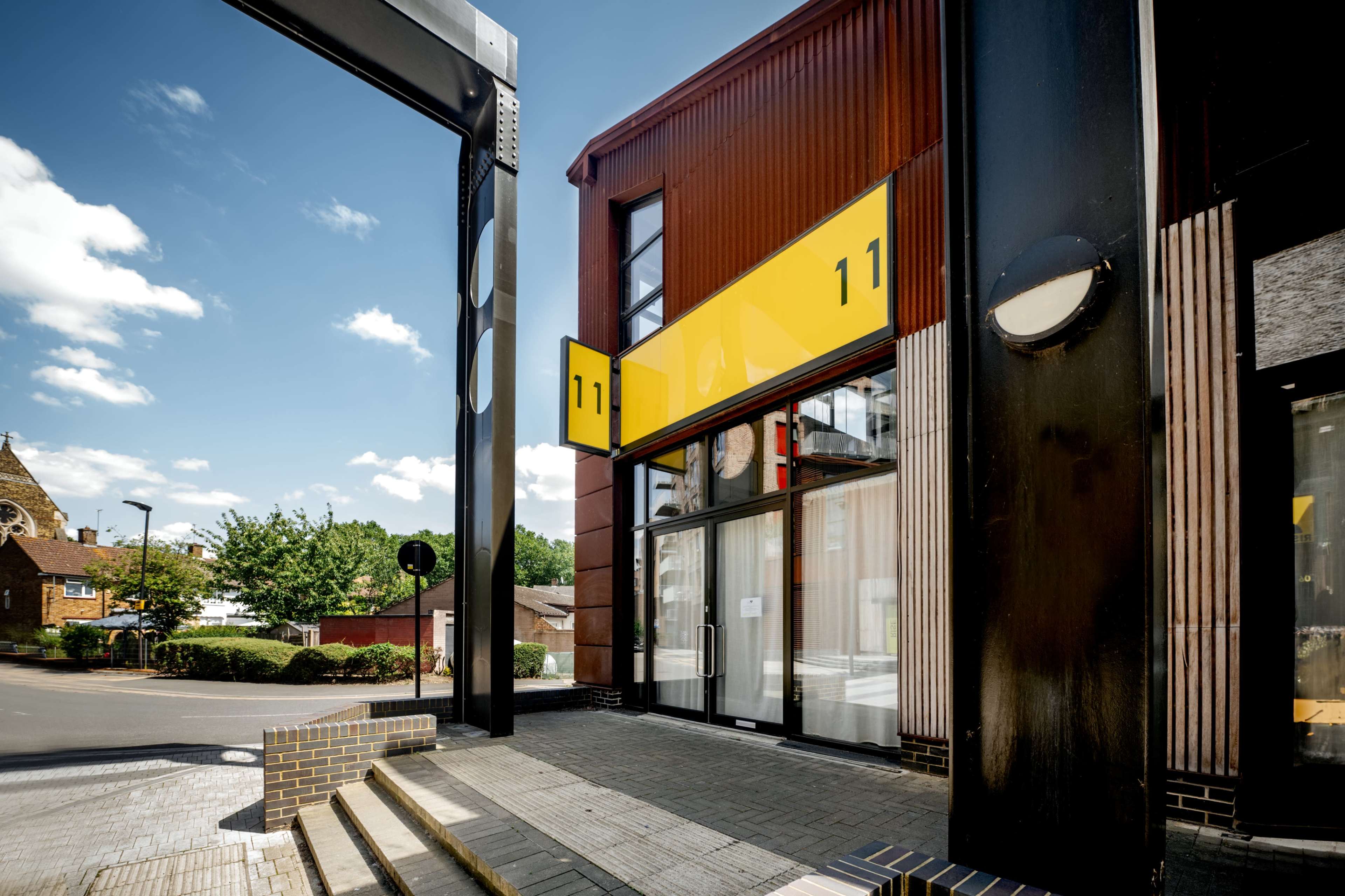 A modern building with a bright yellow facade and large windows is located at the corner of a street, framed by two black pillars.
