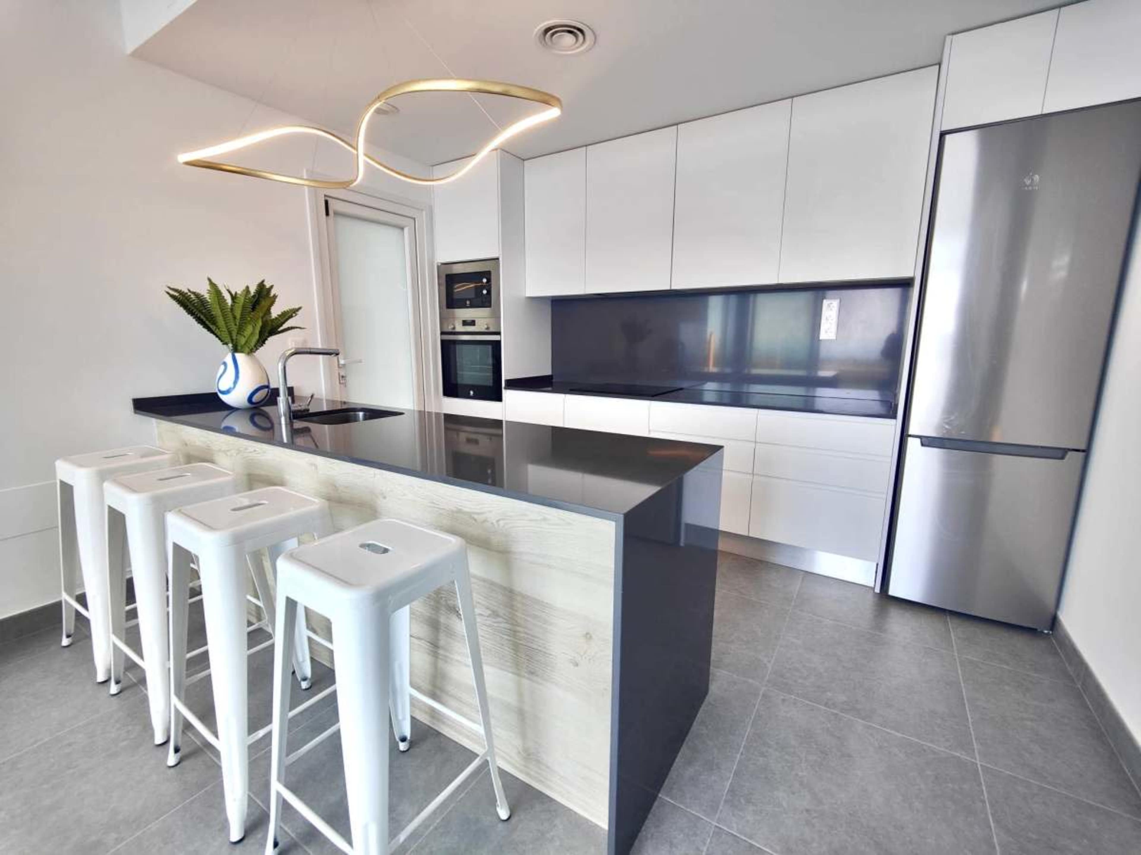 The image shows a modern kitchen featuring a central island with seating, sleek cabinets, and stainless steel appliances.