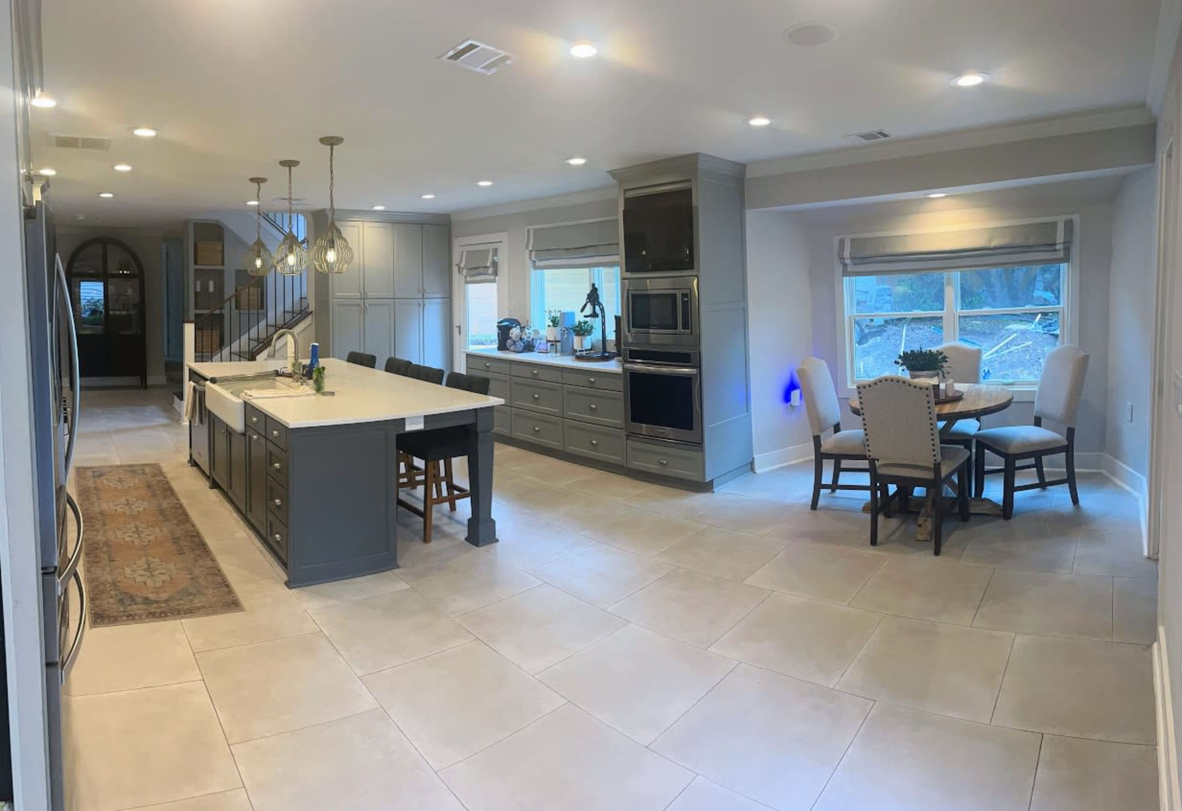 The image shows a modern kitchen with an island, gray cabinetry, stainless steel appliances, and a dining area with a round table and four chairs.
