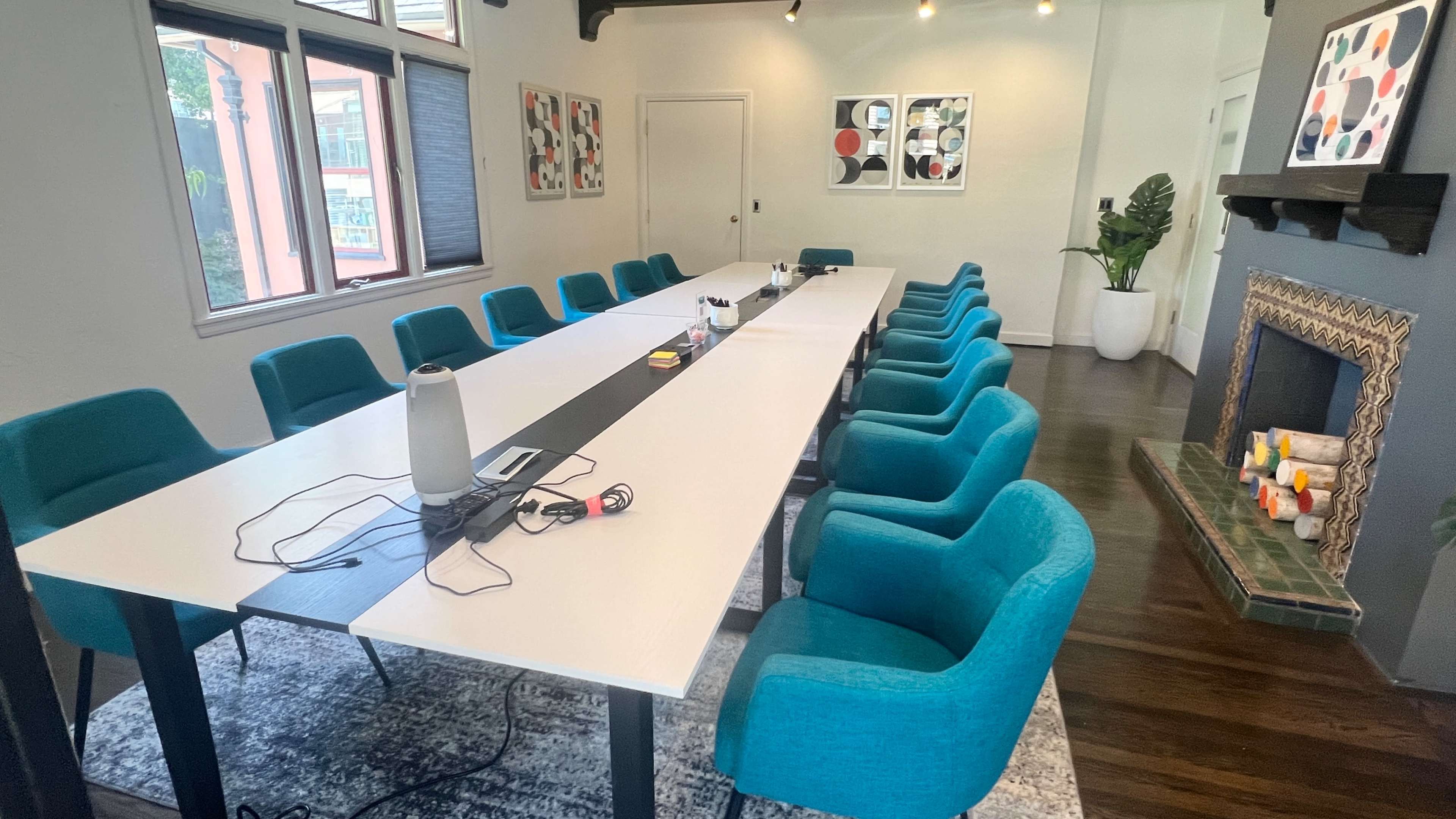 A large conference room features a long white table surrounded by teal chairs, a fireplace, and artwork on the walls.