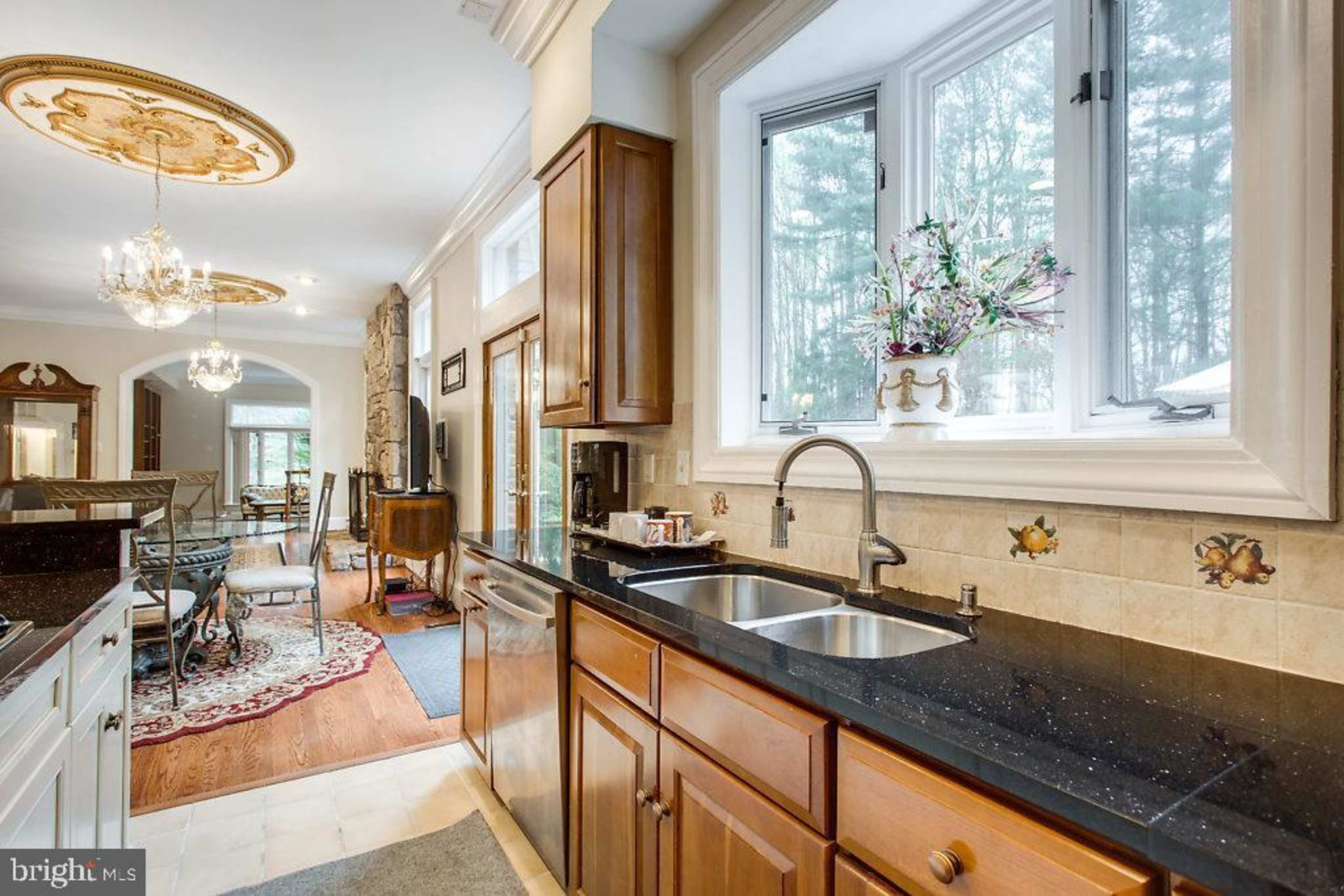 A kitchen with dark wood cabinets, a double sink, and large windows overlooking a wooded area.