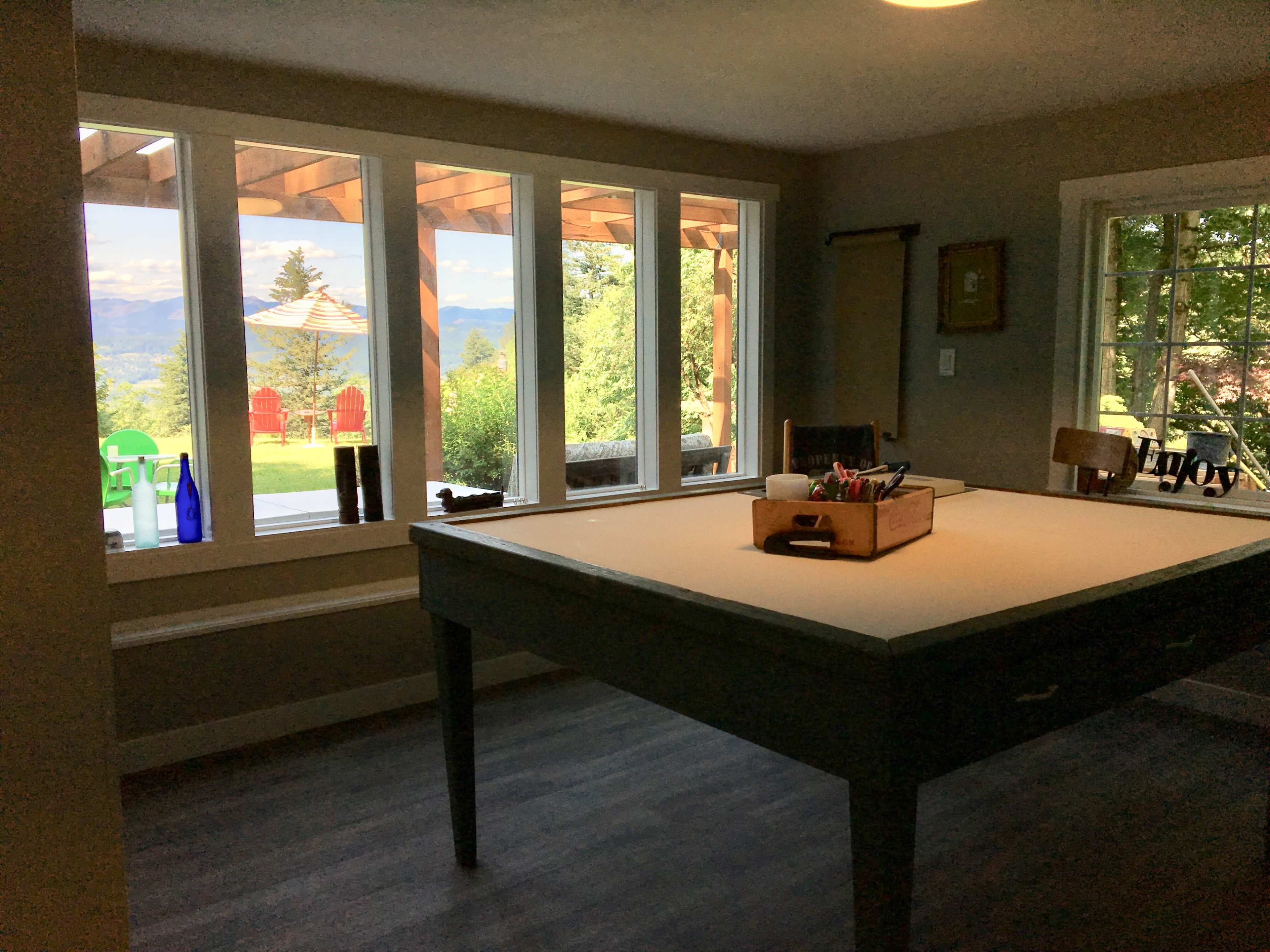 A large table with a box of supplies sits in a brightly lit room featuring large windows that overlook a scenic outdoor area.