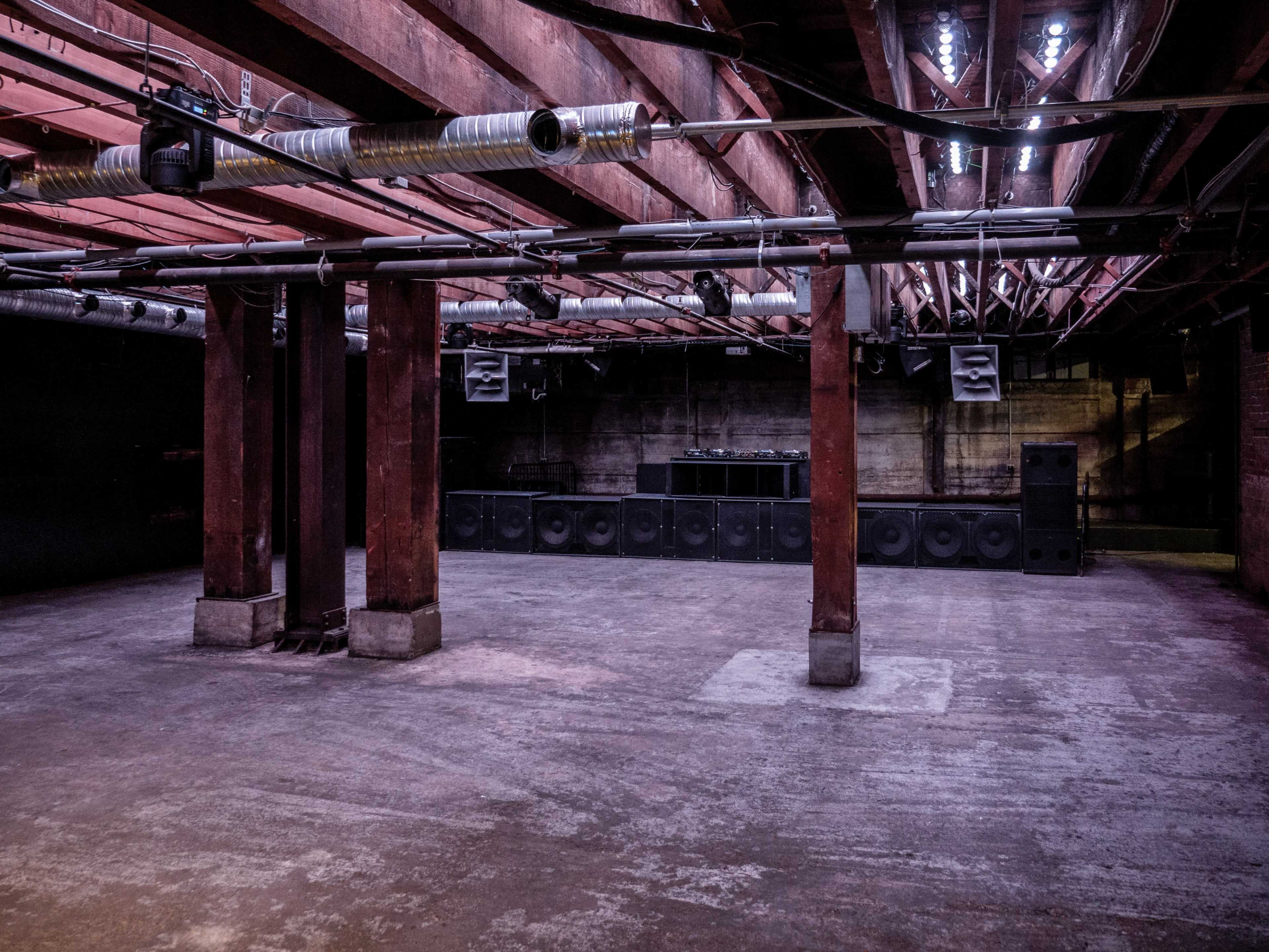An empty industrial space with exposed wooden beams and a sound system set up against one wall.