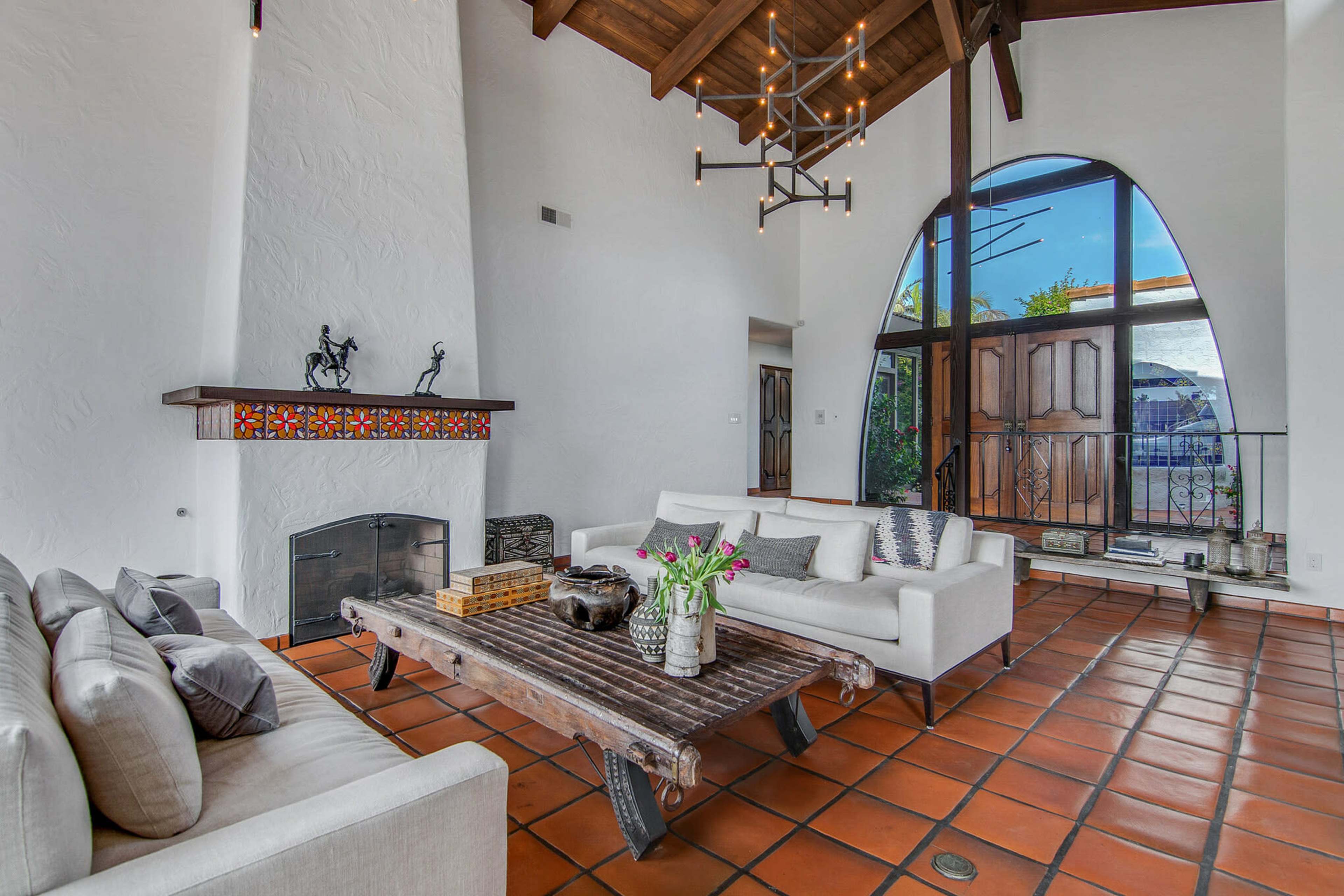 A spacious living room with a high ceiling, a large wooden coffee table, and a fireplace, featuring arched windows that allow natural light to enter.