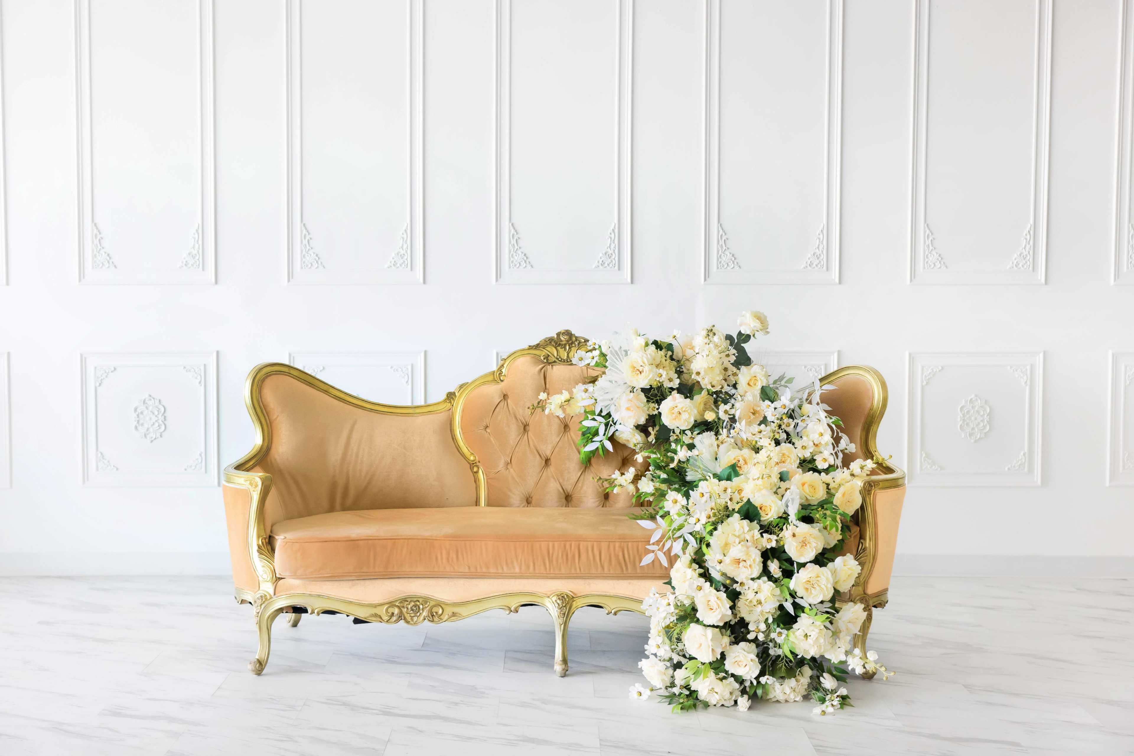 A vintage-style sofa with a golden frame is adorned with an arrangement of white flowers cascading over one side.