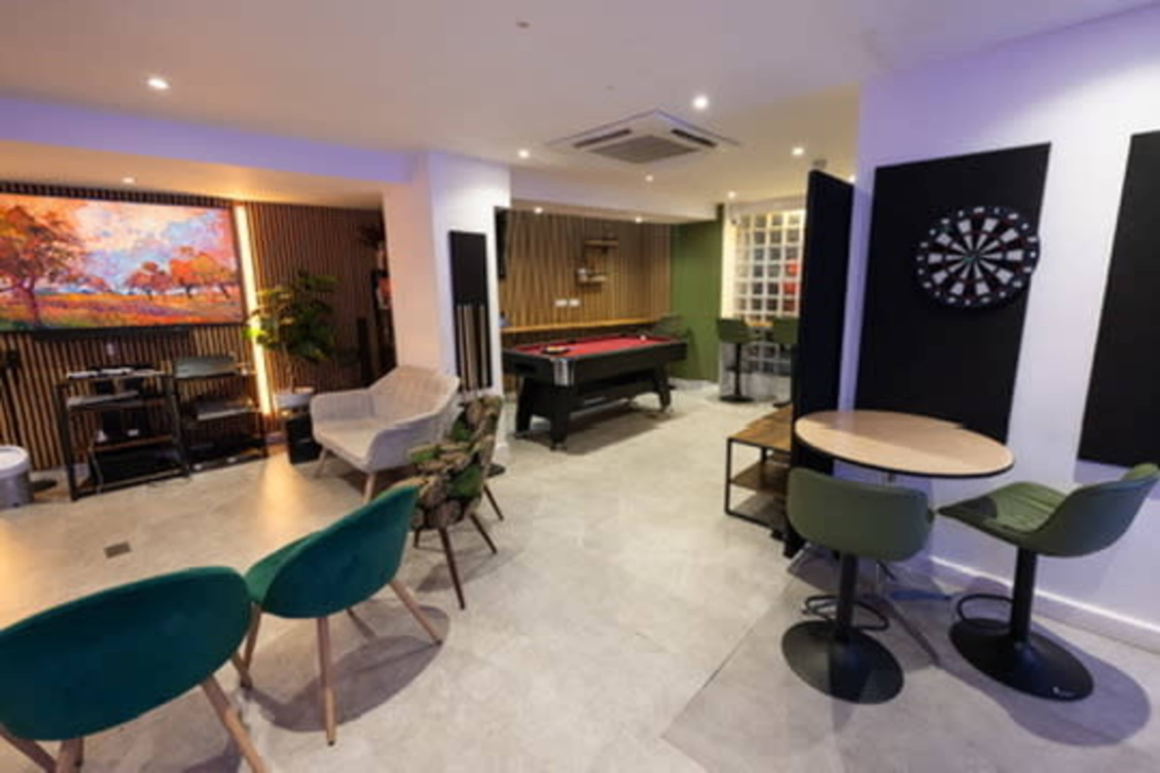 The image shows a modern lounge area featuring a pool table, seating arrangements, a dartboard, and decorative wall art.