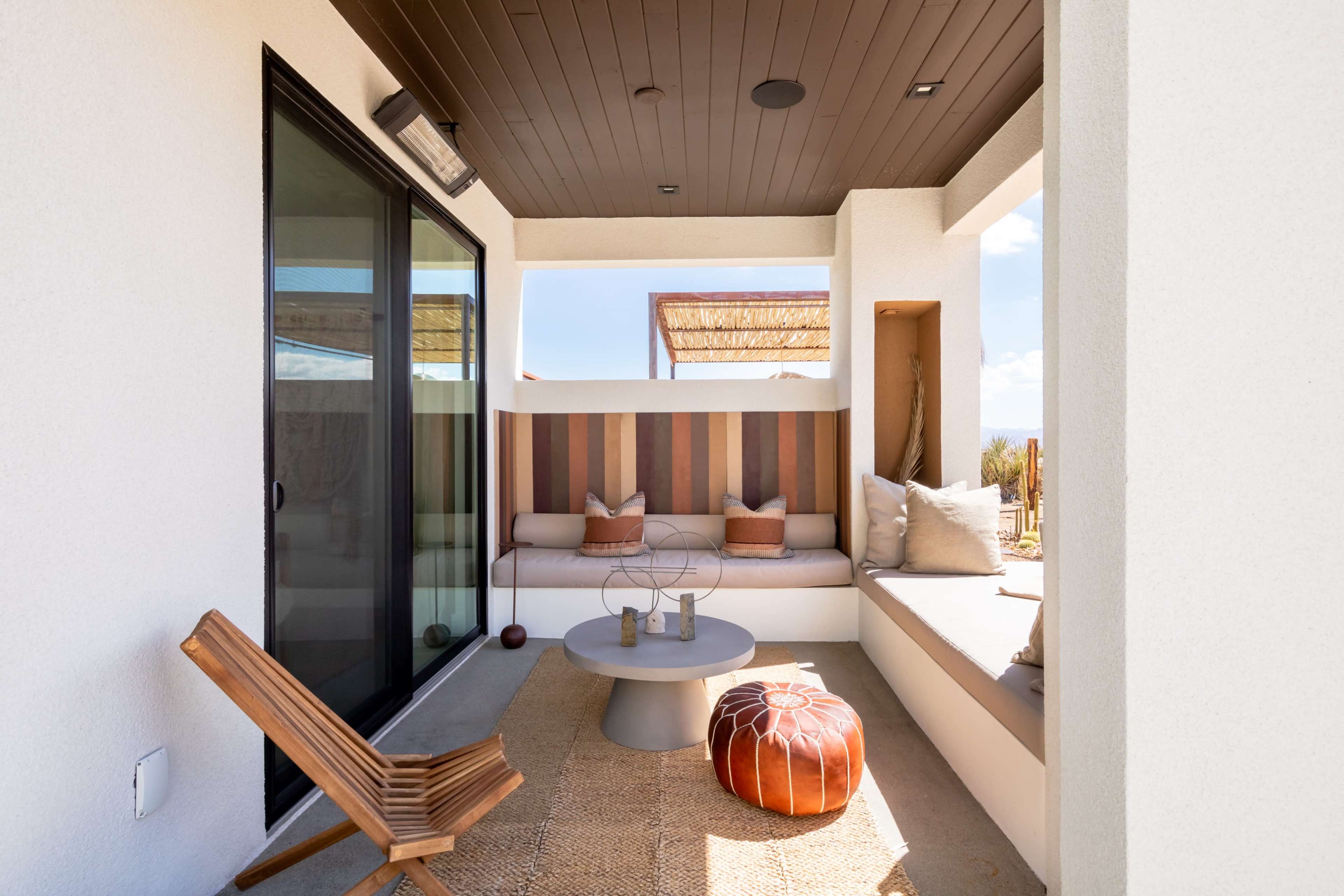 A modern, outdoor lounge area with a seating space, a round table, and a wooden chair.