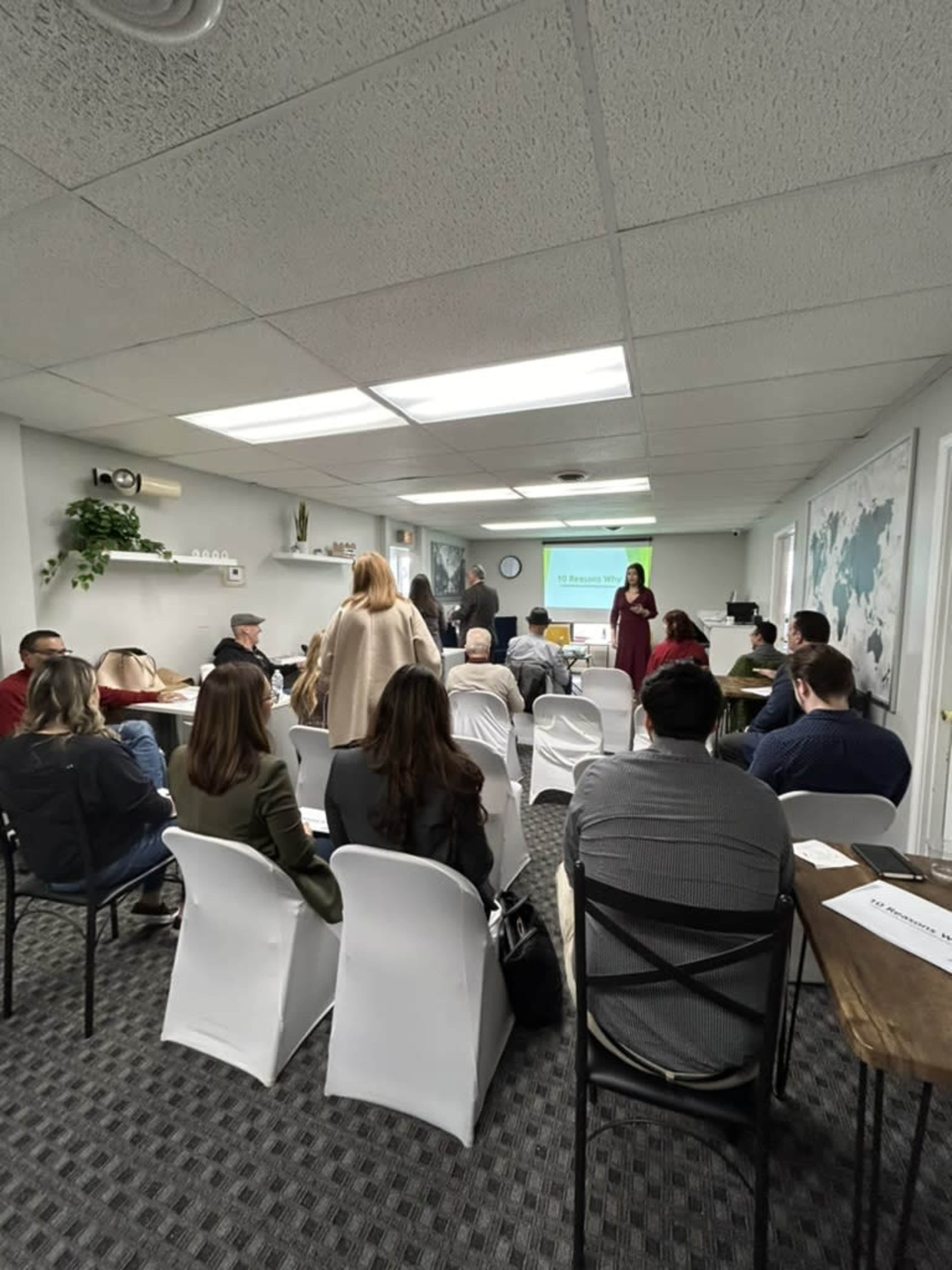 A group of people is seated in a conference room, watching a presentation displayed on a screen at the front.