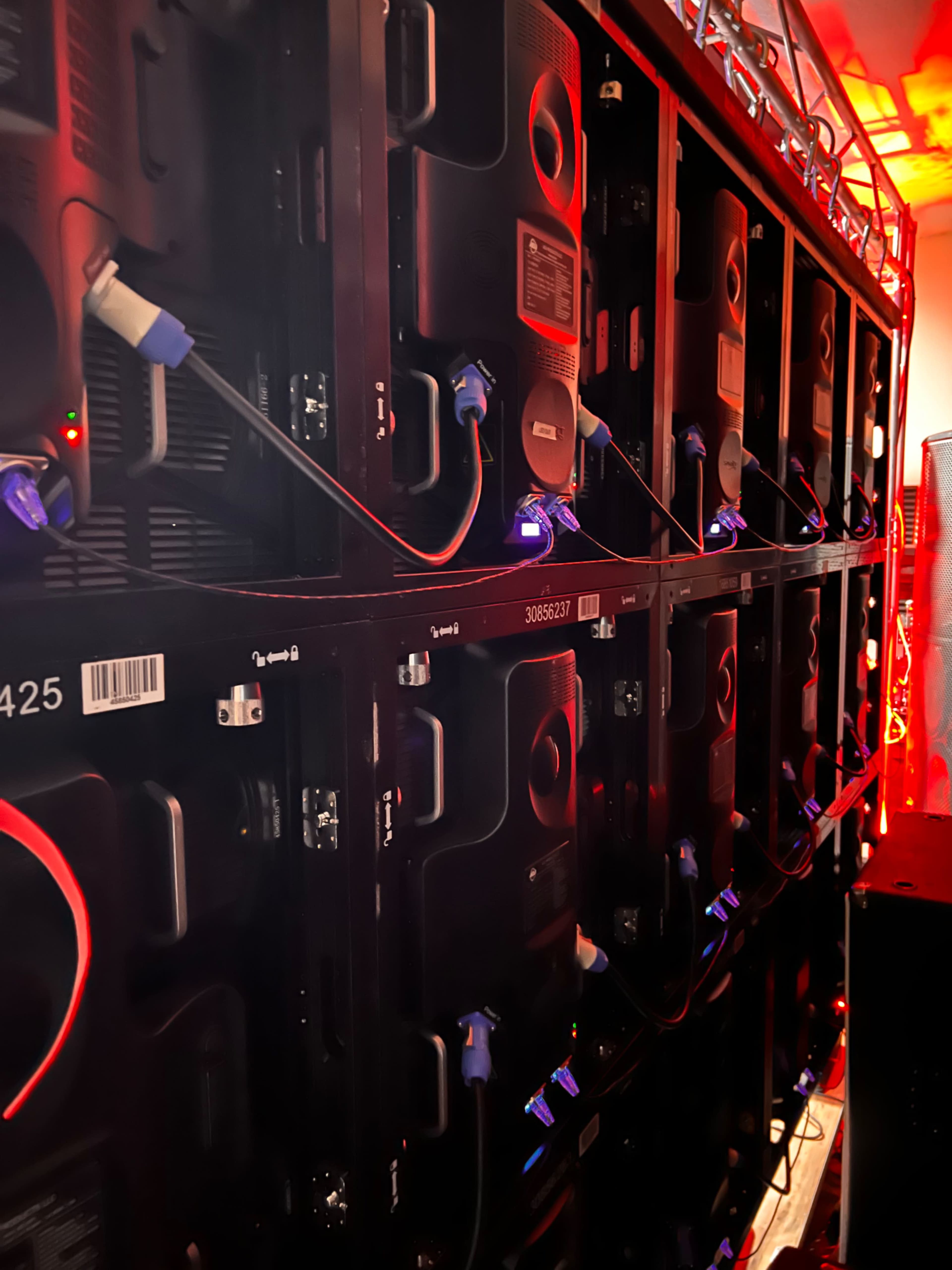 A series of stacked black display screens are connected by cables and illuminated by red lighting.