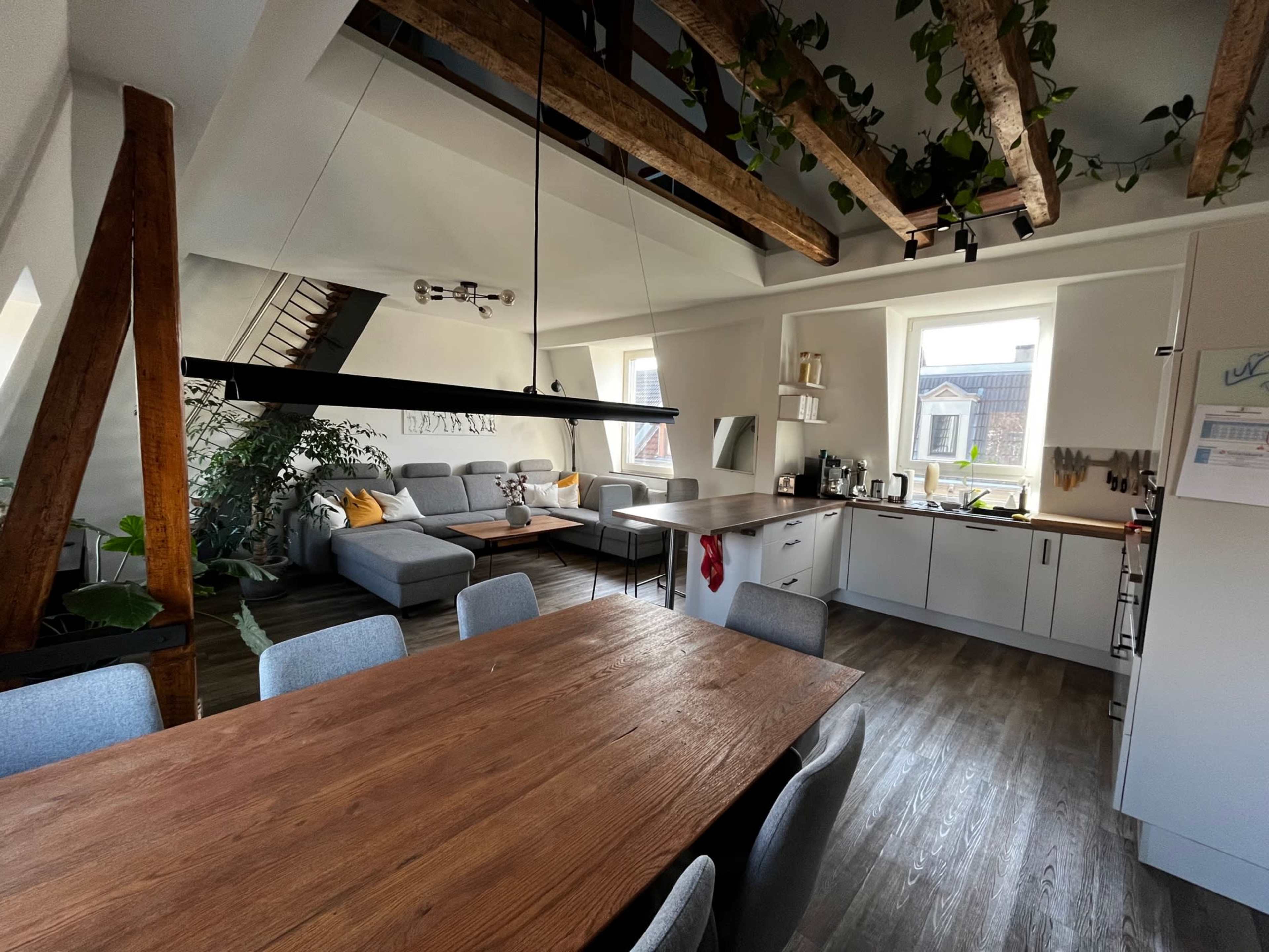 A modern kitchen and dining area featuring wooden beams, a large dining table, and a spacious gray couch.