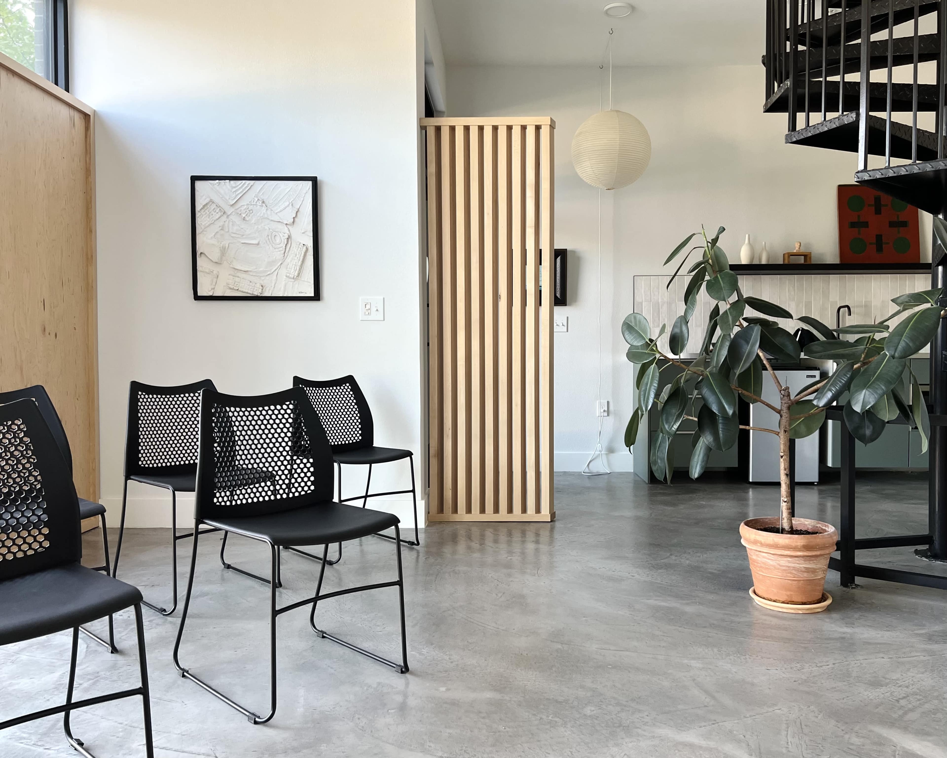 The interior features a minimalist seating area with black chairs, a potted plant, and a wooden partition separating the space.