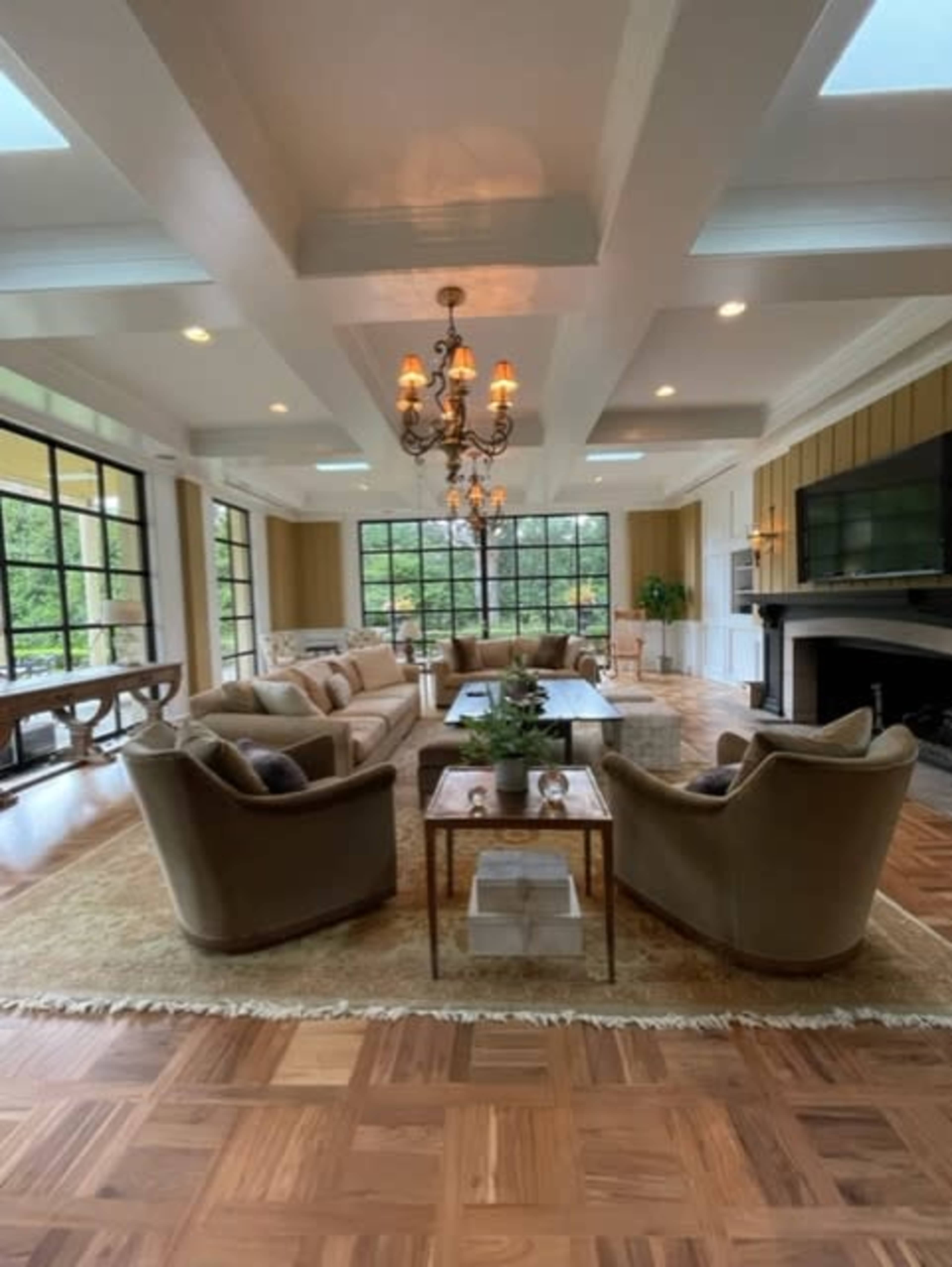 A spacious, well-lit living room with a large window, comfortable seating, and a modern chandelier.