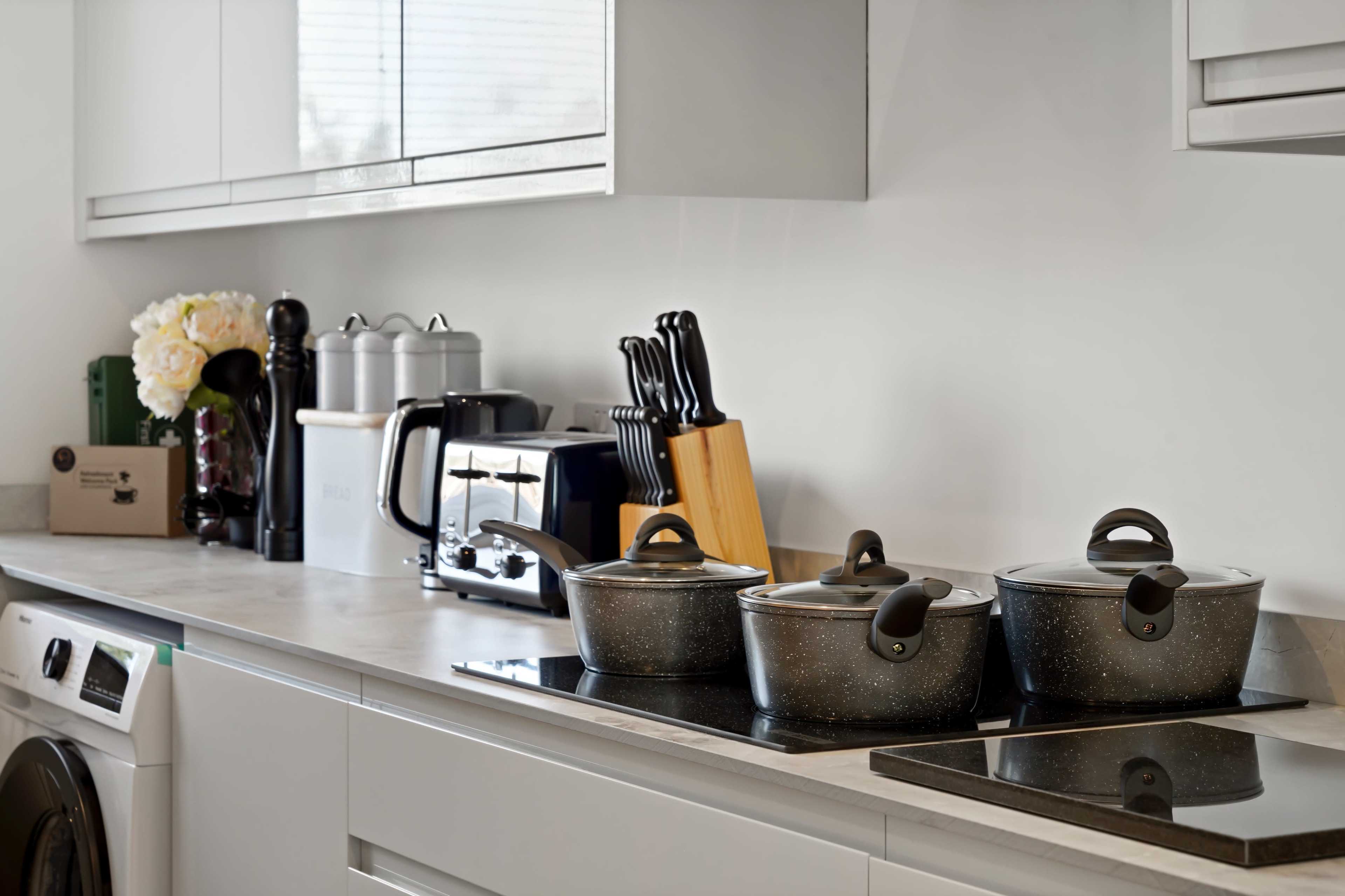 A modern kitchen counter features three pots, a toaster, a knife block, and a washing machine.
