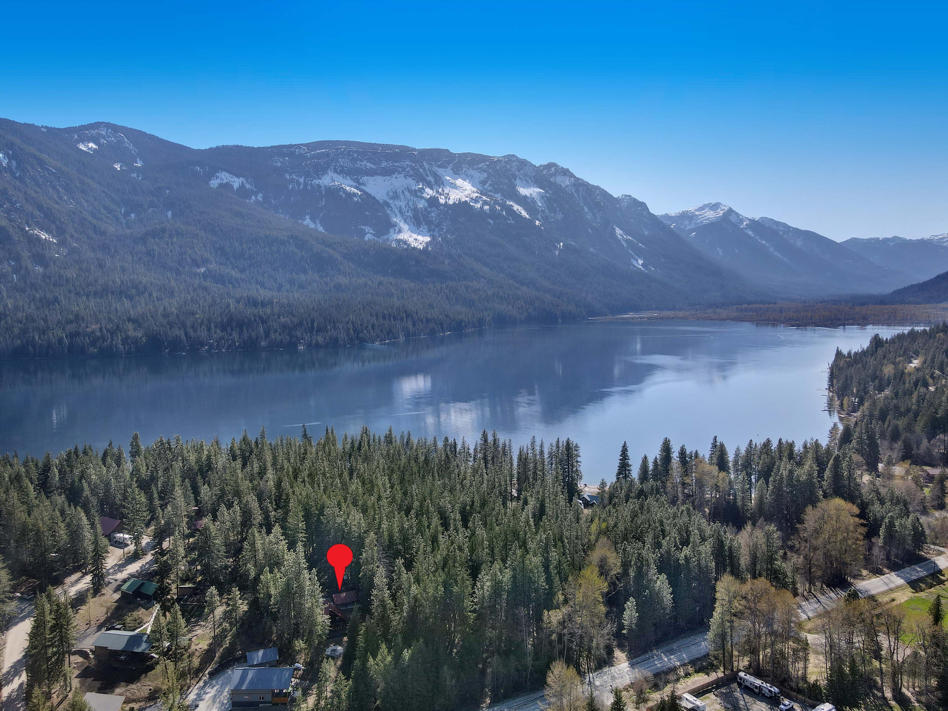 An aerial view shows a clear lake surrounded by dense forests and mountains, with a road visible in the foreground.
