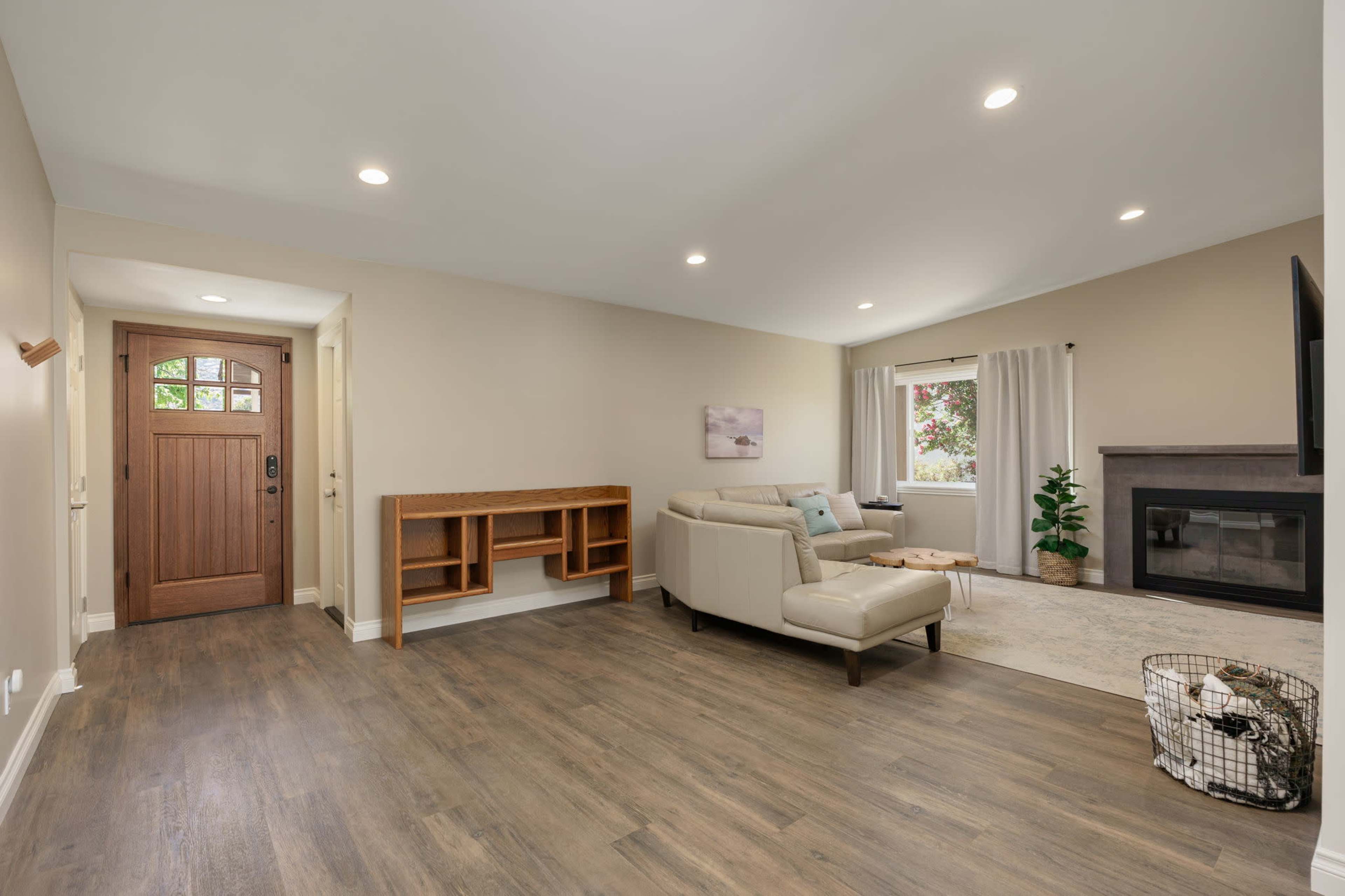 The image depicts a bright living room with a light-colored couch, a fireplace, a front door, and a small shelving unit against the wall.