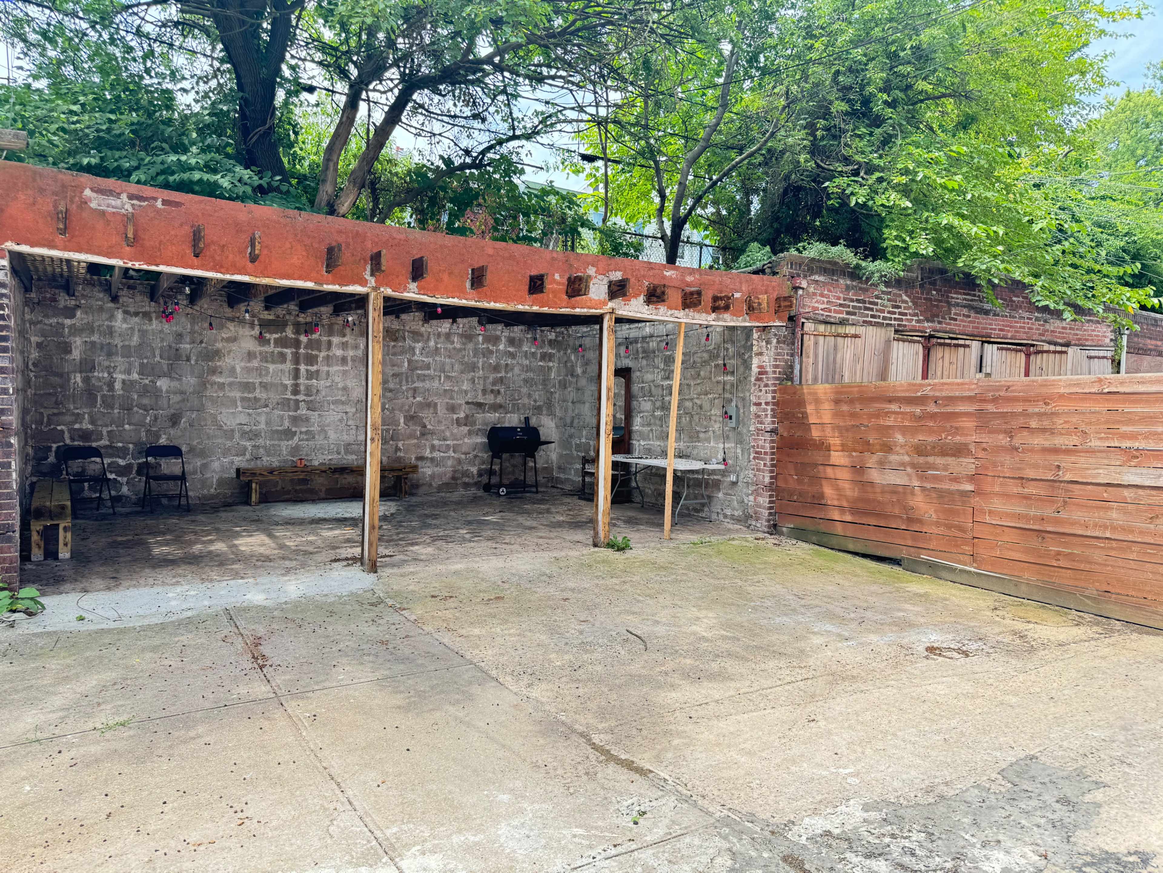 A partially open outdoor space with a concrete floor, a stone wall in the background, and wooden fencing on one side.