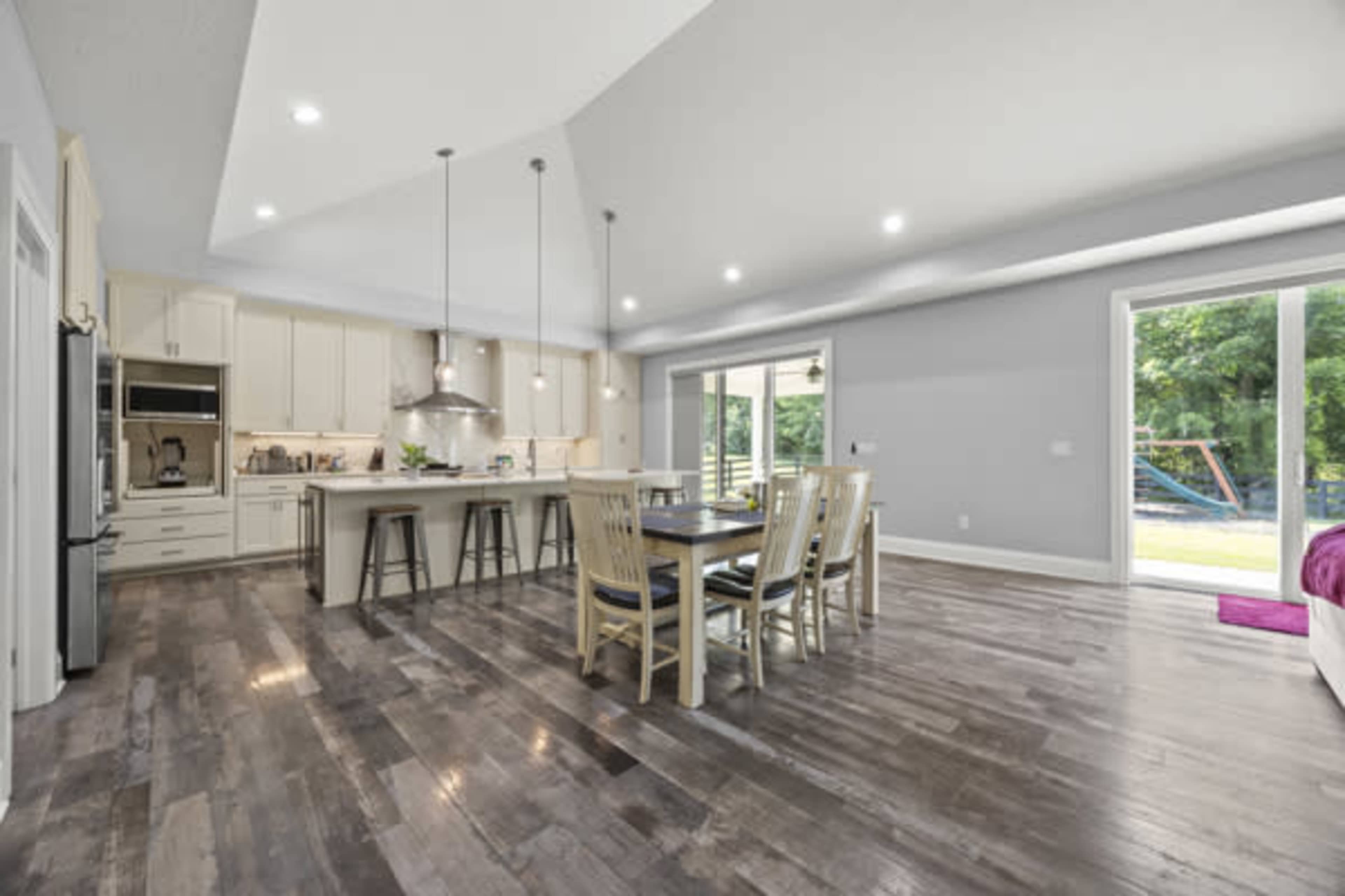 The image shows a modern kitchen and dining area with wooden flooring, a large island, and sliding glass doors leading to an outdoor space.
