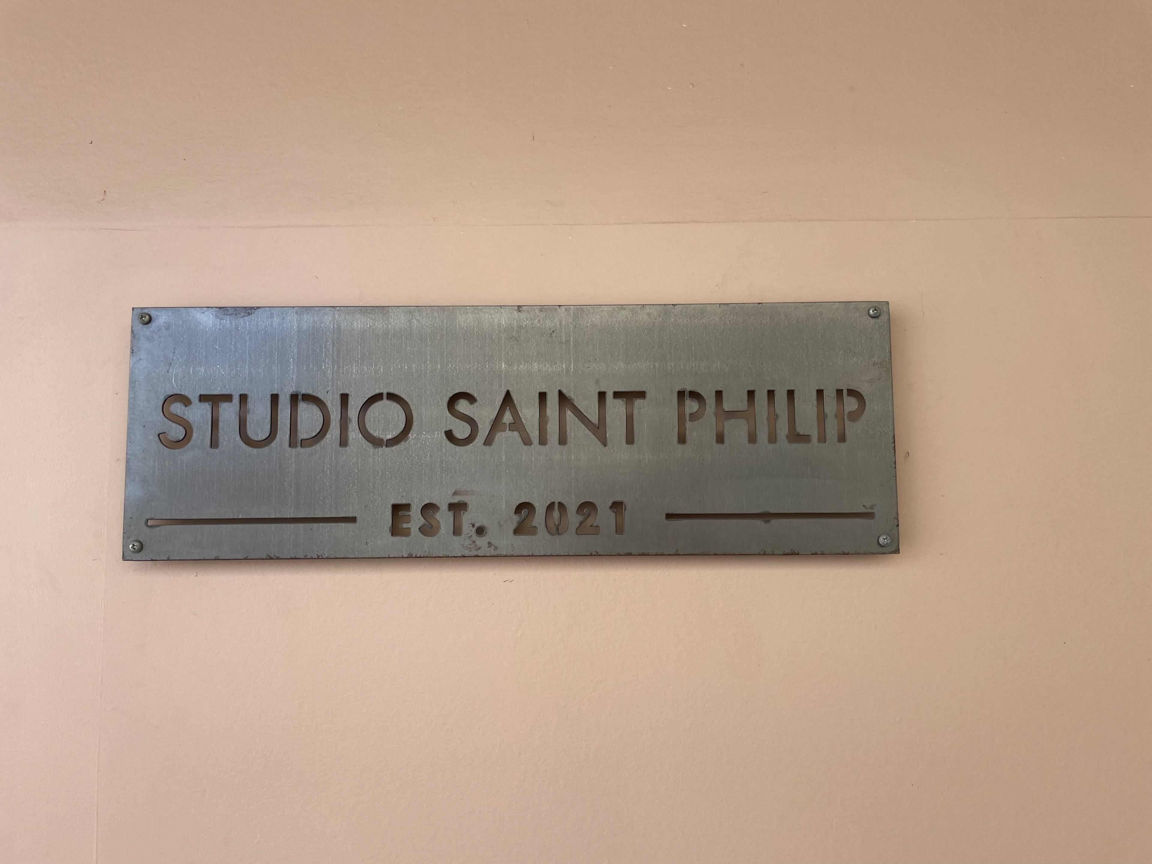 A metal sign on a wall displays the text "STUDIO SAINT PHILIP" with "EST. 2021" below it.