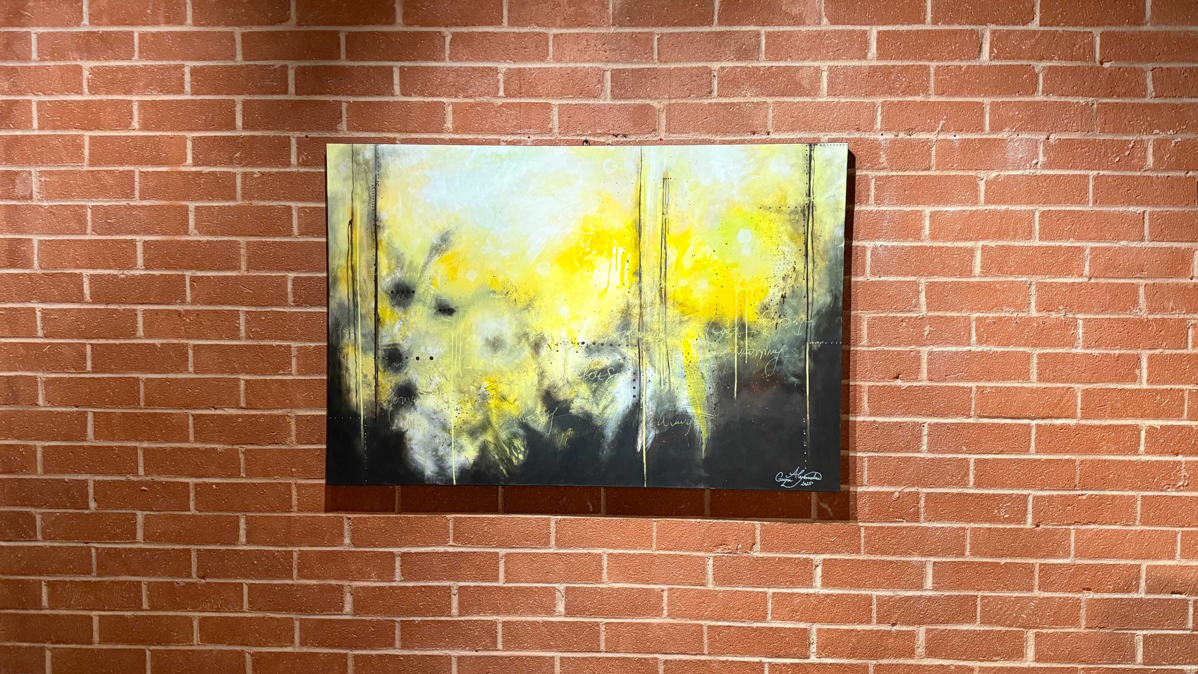 A colorful abstract painting featuring yellow and black hues is hung on a brick wall.