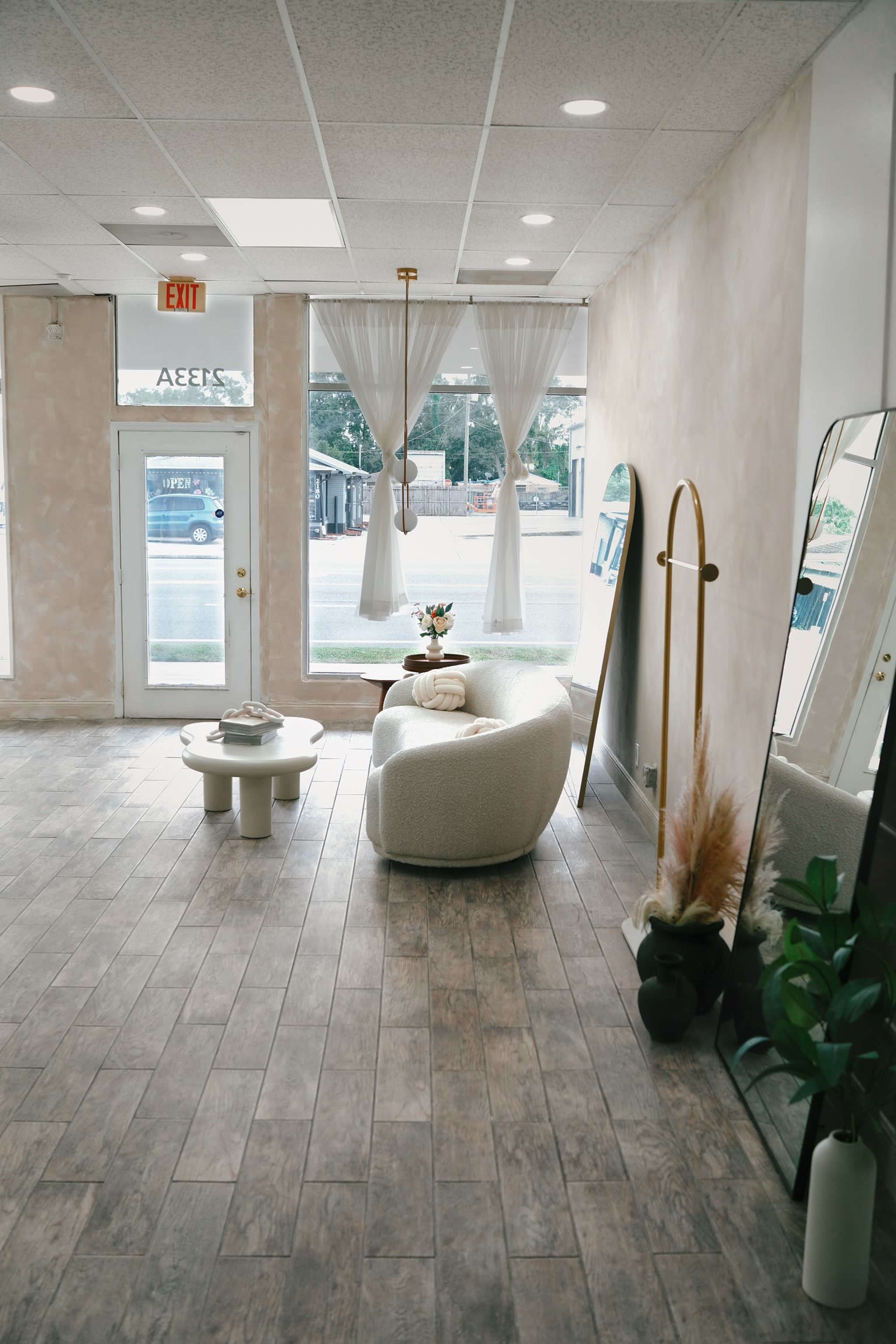 A minimalist interior of a shop with a light-colored wall, a curved couch, a small coffee table, and large windows allowing natural light to enter.