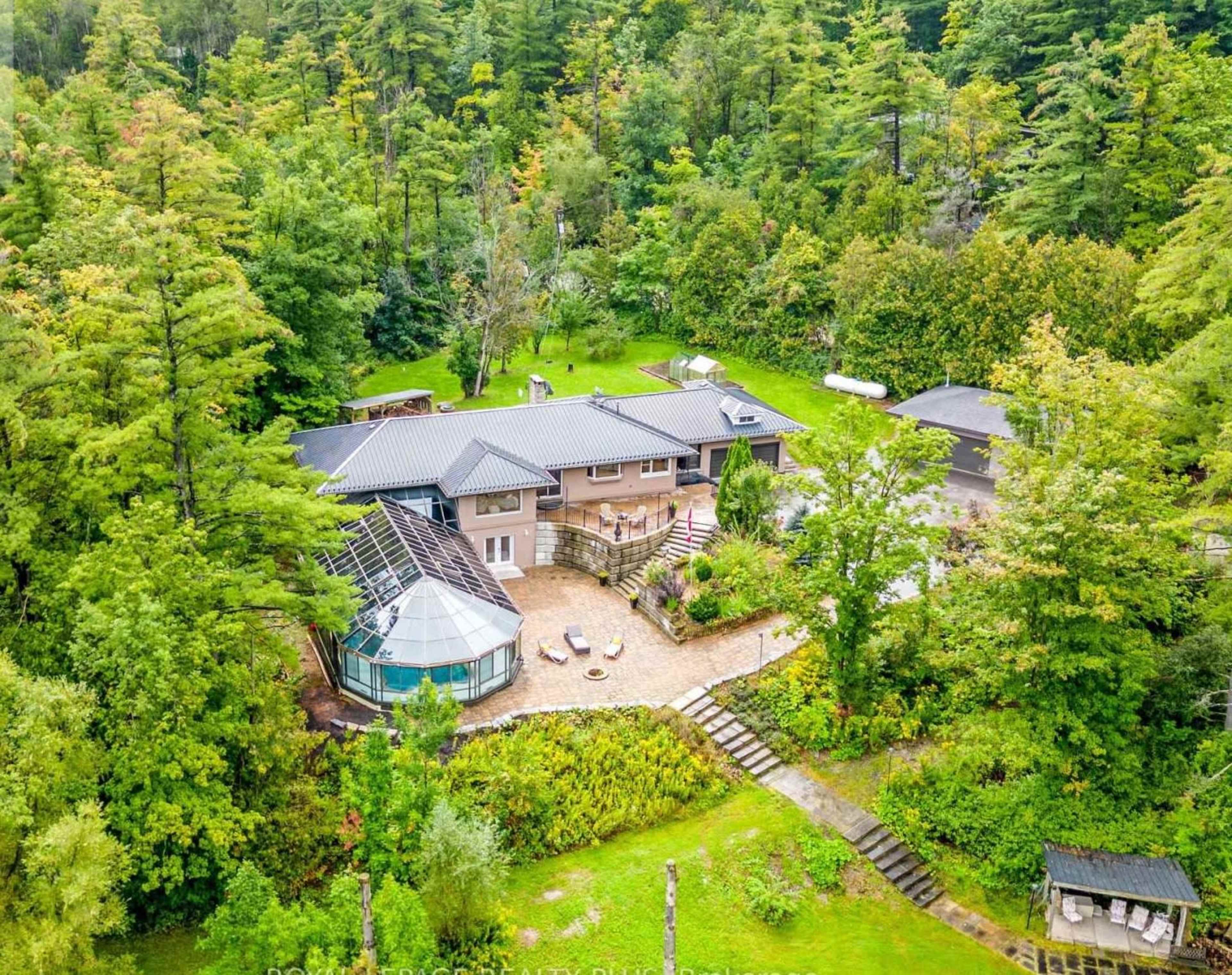 The image shows a large, modern house surrounded by lush greenery and trees, with a patio area and a gazebo in the outdoor space.