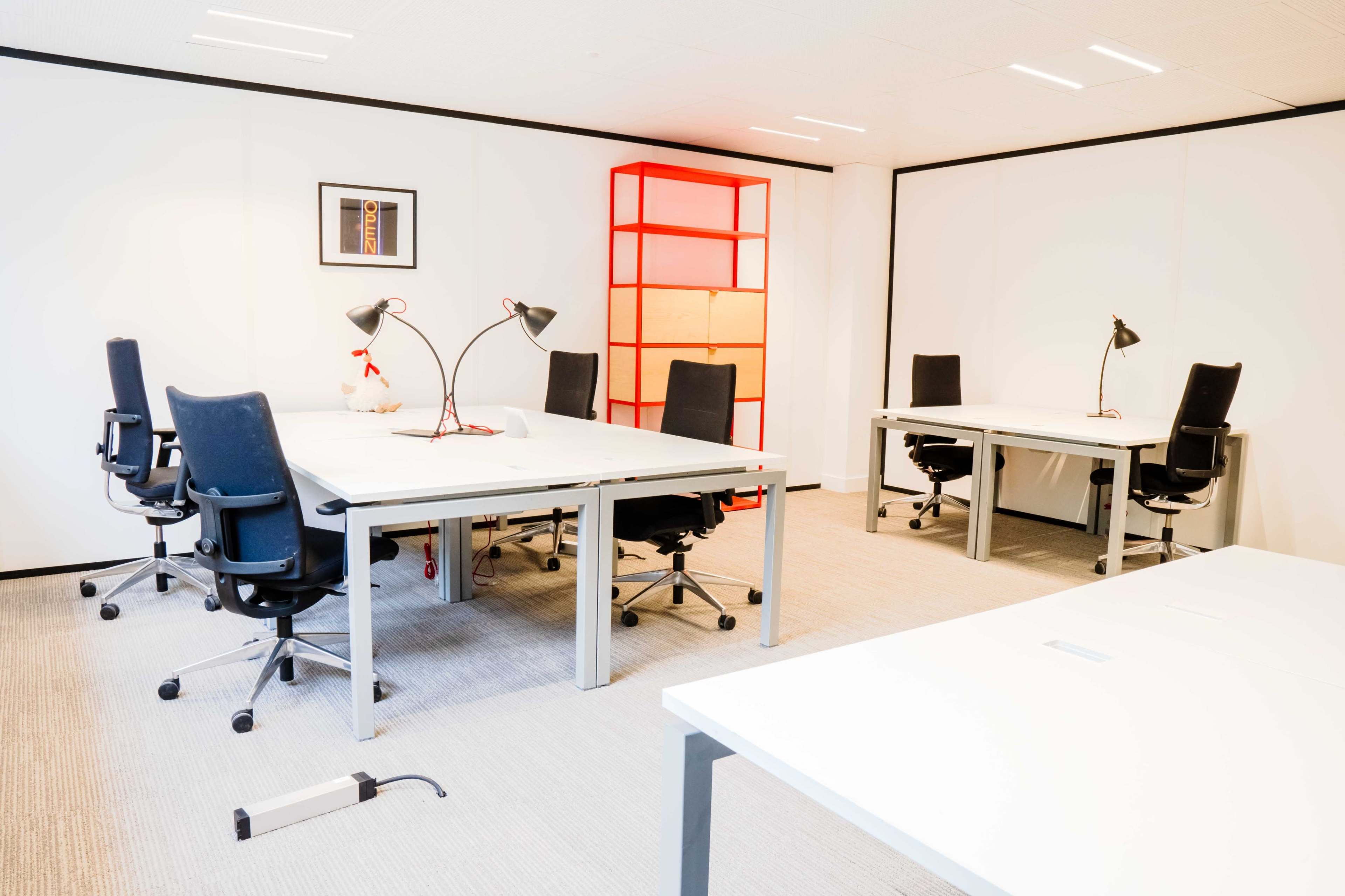 The image shows a modern office space with multiple white desks, black office chairs, and a red shelf, illuminated by desk lamps.