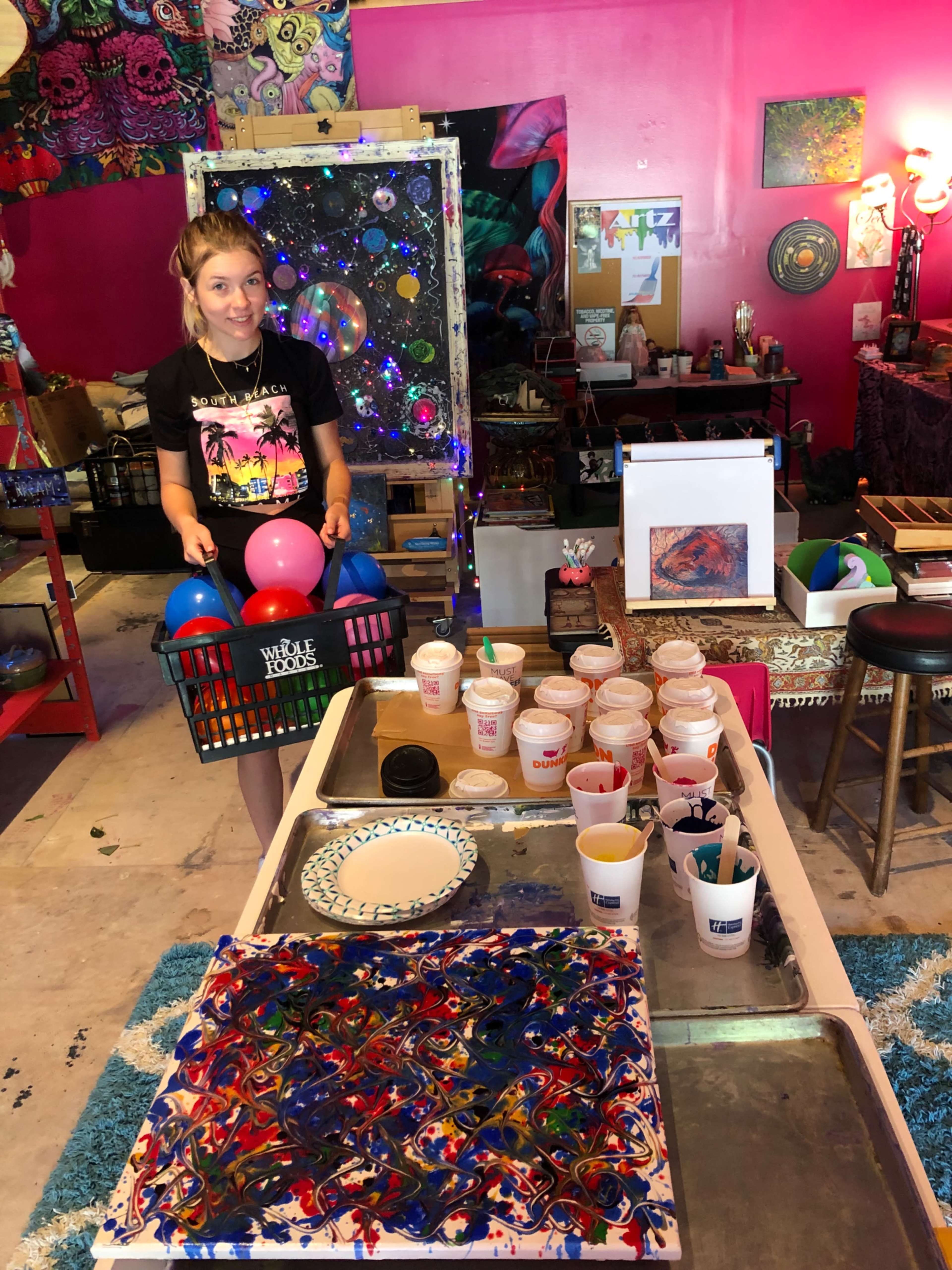 A person holds a basket of colored balls in an art studio filled with vibrant decorations and various art supplies.