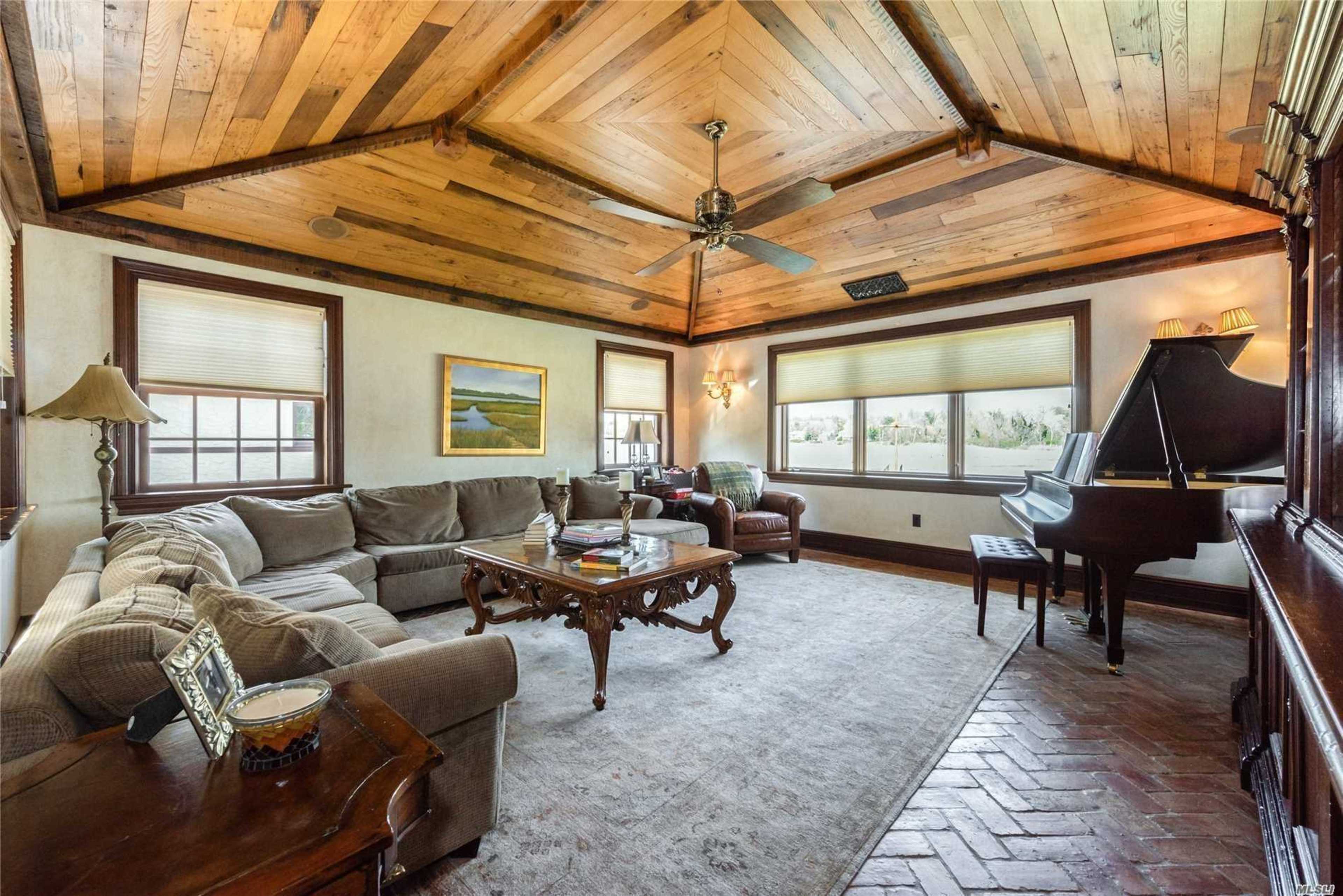 A cozy living room featuring a wooden ceiling, a grand piano, a large sectional sofa, and a coffee table set on a patterned rug.