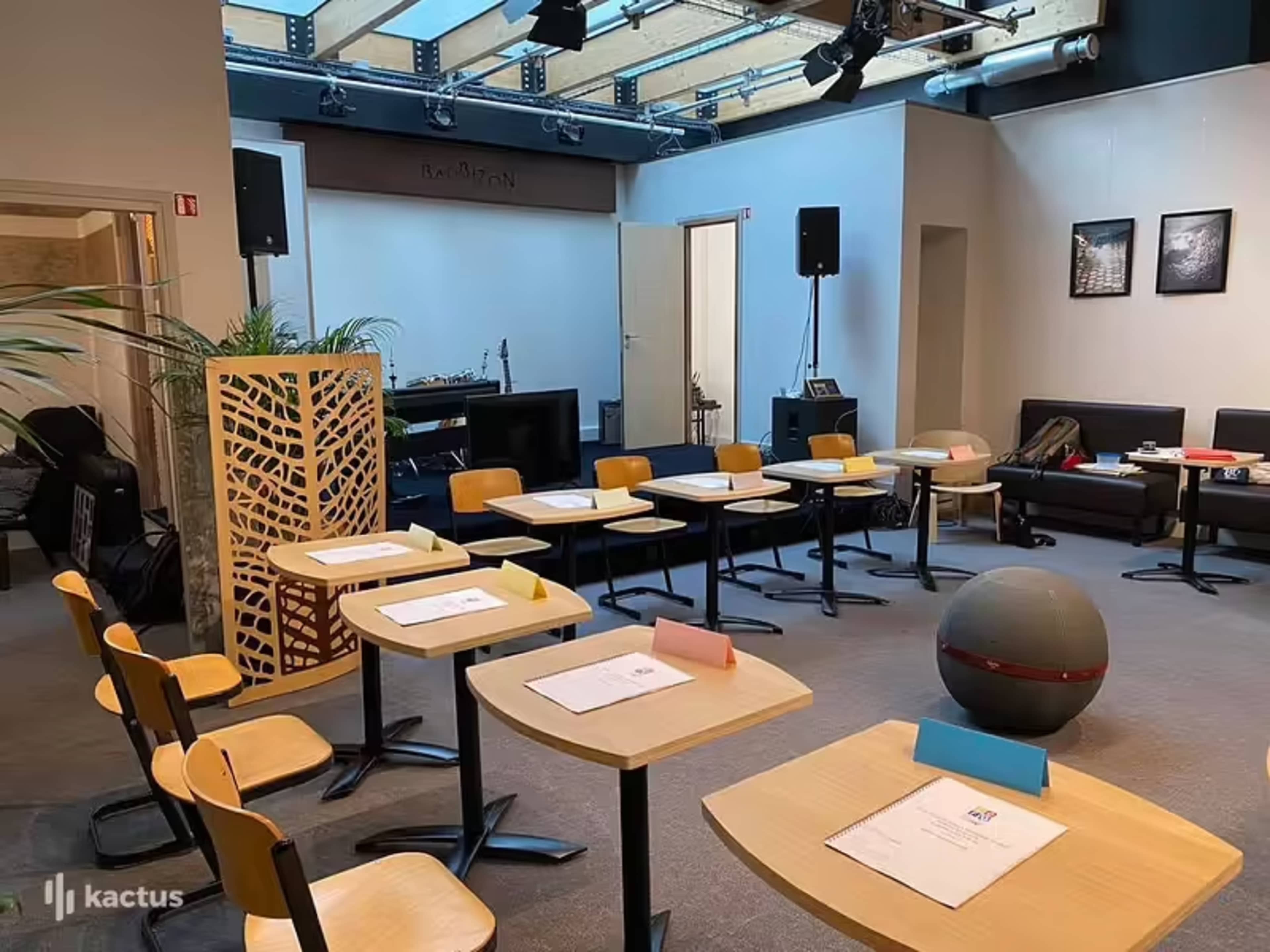 The room is set up with several tables and chairs arranged for a meeting or event, with sound equipment and a stage area in the background.