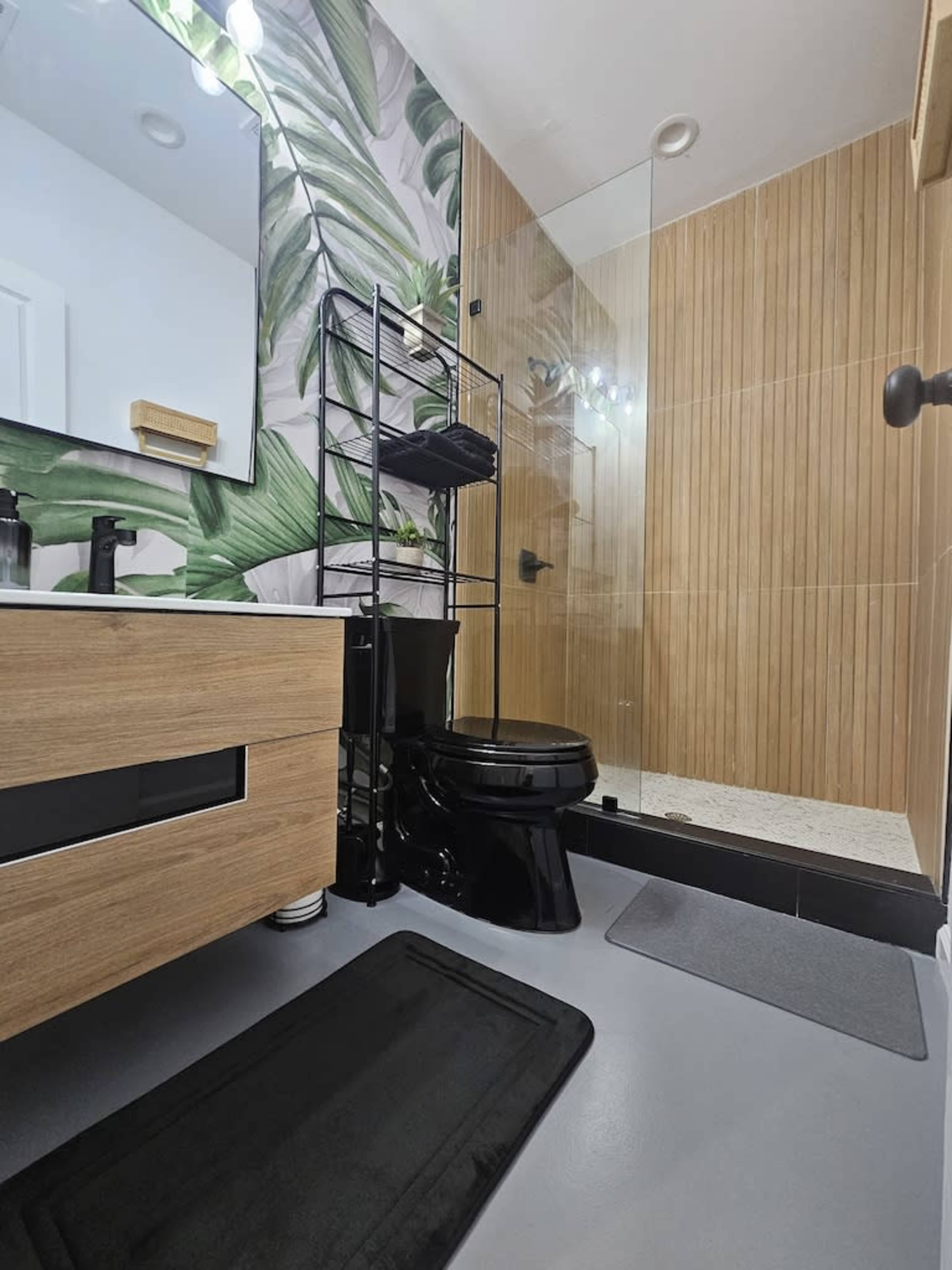 A modern bathroom with a glass shower, wooden wall accents, a black toilet, and a stylish vanity.