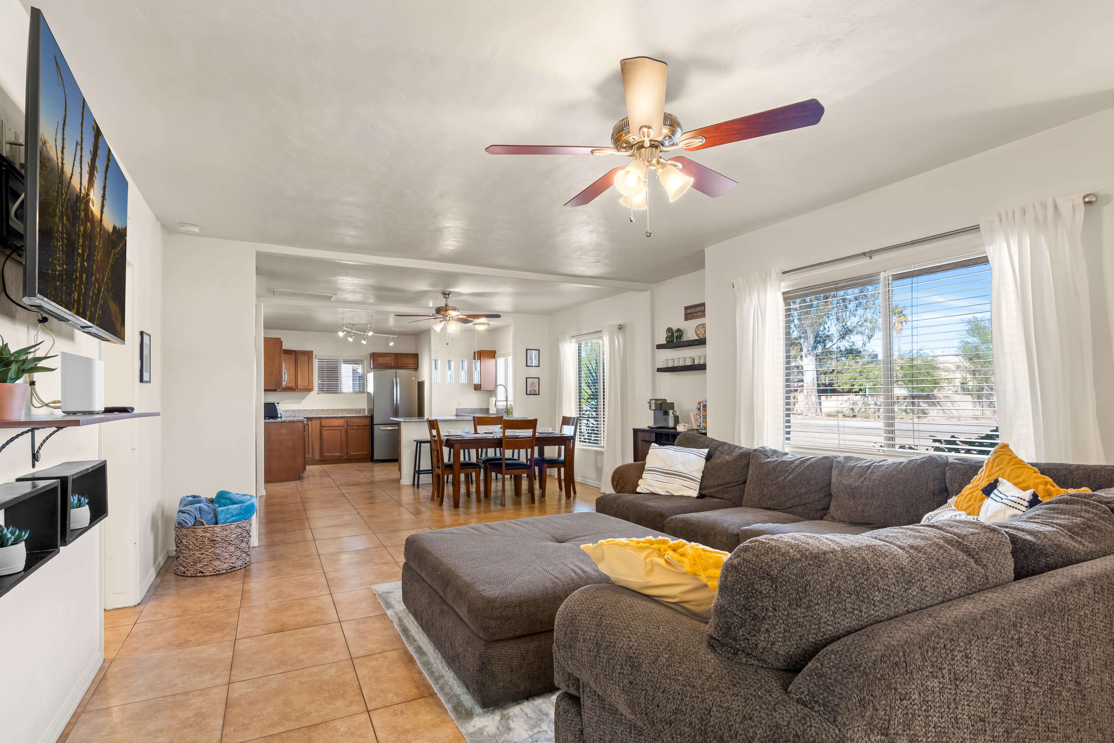 A spacious living room featuring a large sectional sofa, a ceiling fan, and an open layout leading to a kitchen and dining area.