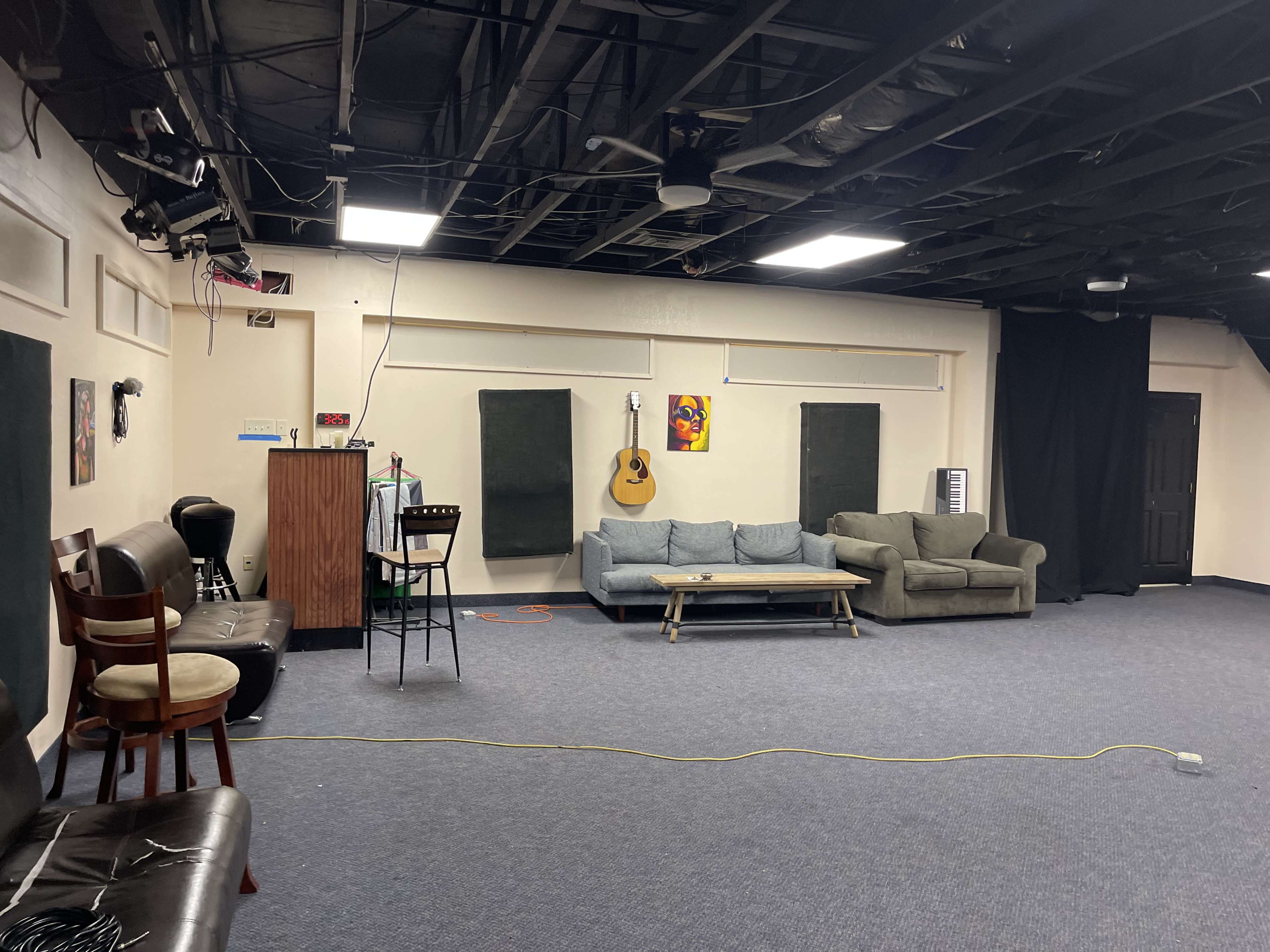 The image shows a spacious room with a couch, an acoustic guitar hanging on the wall, and various seating arrangements.