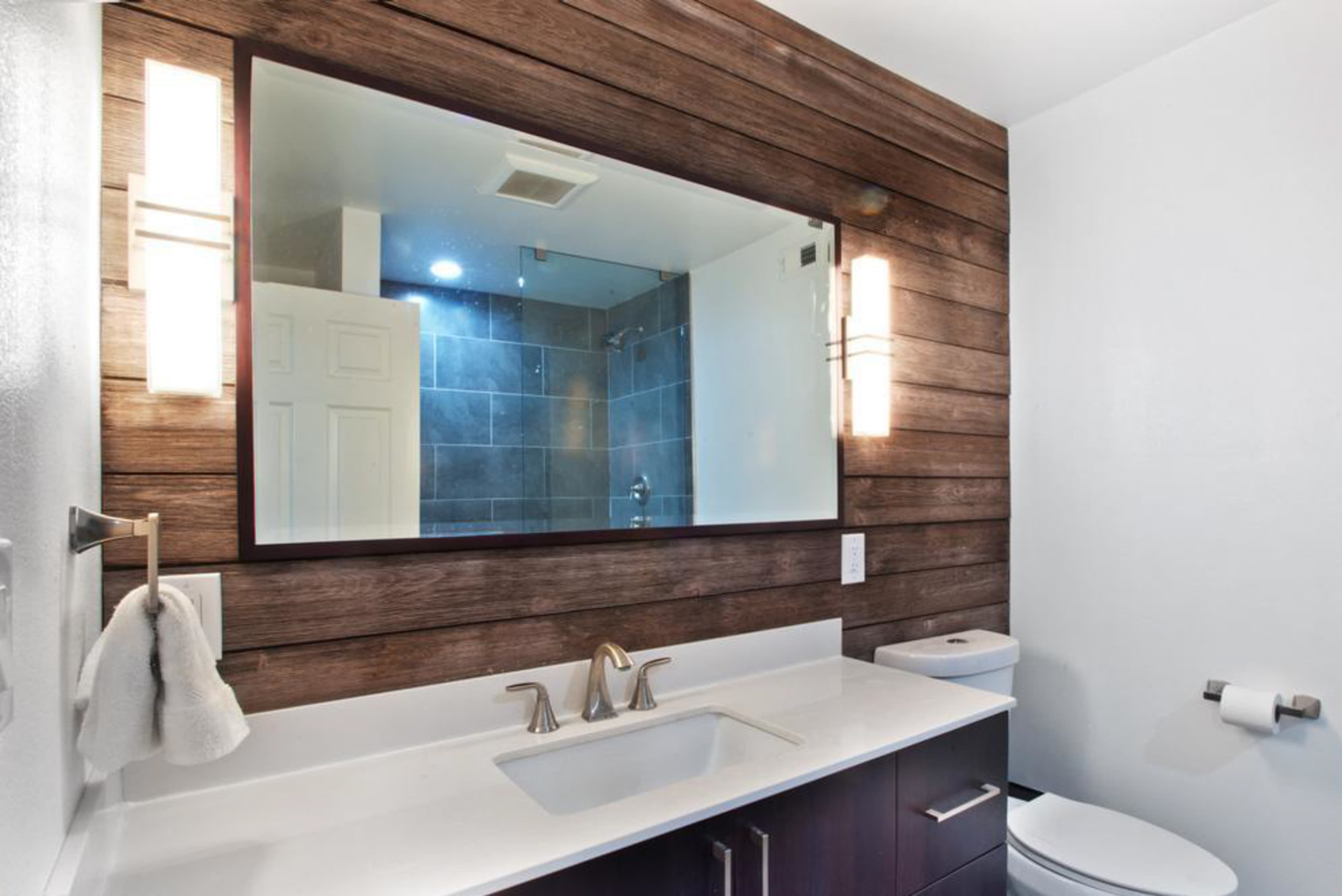 A modern bathroom with a double sink vanity, wood-paneled wall, and a large mirror above the sink.