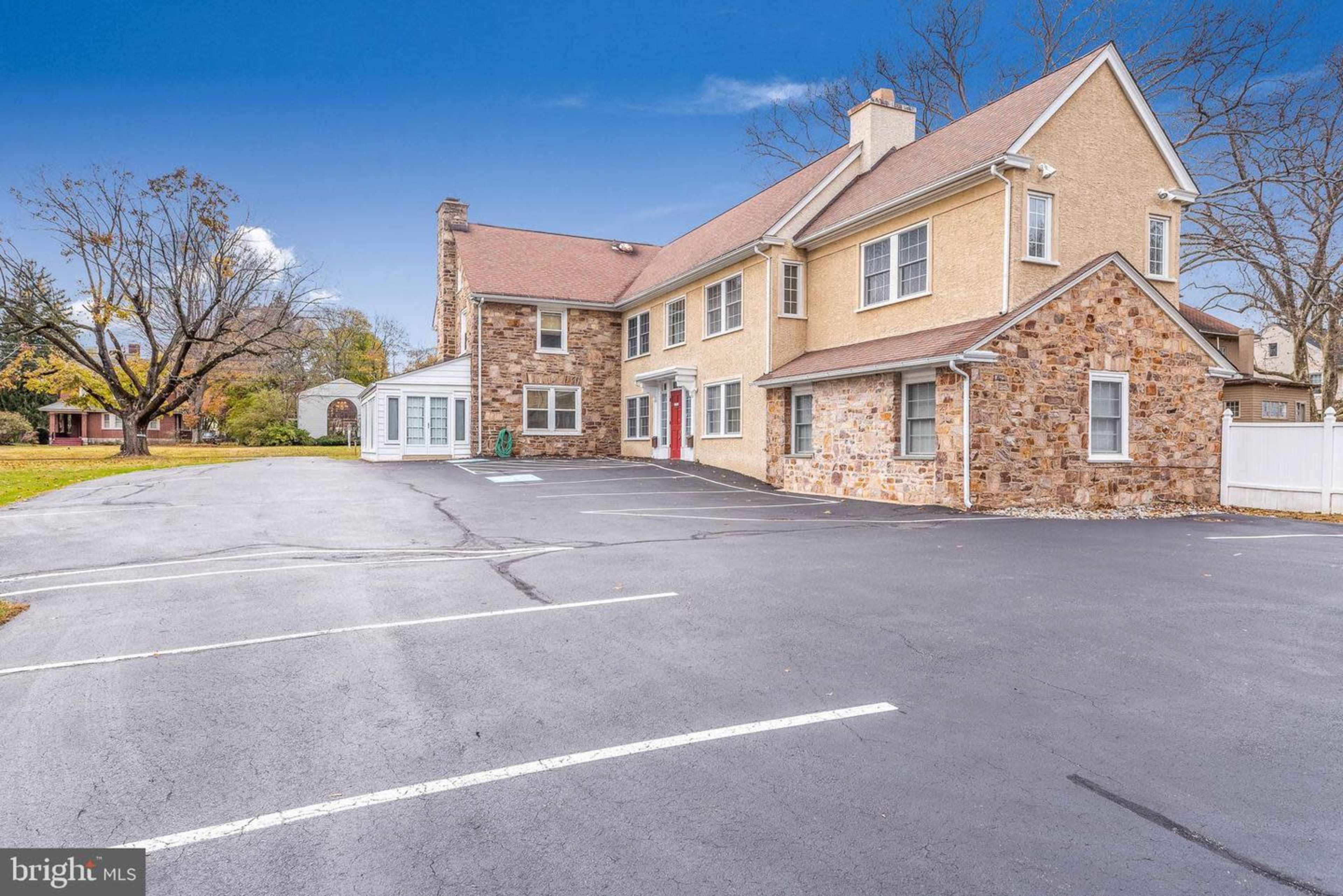 The image shows a two-story building with a stone and stucco exterior, surrounded by a parking lot with several marked spaces.