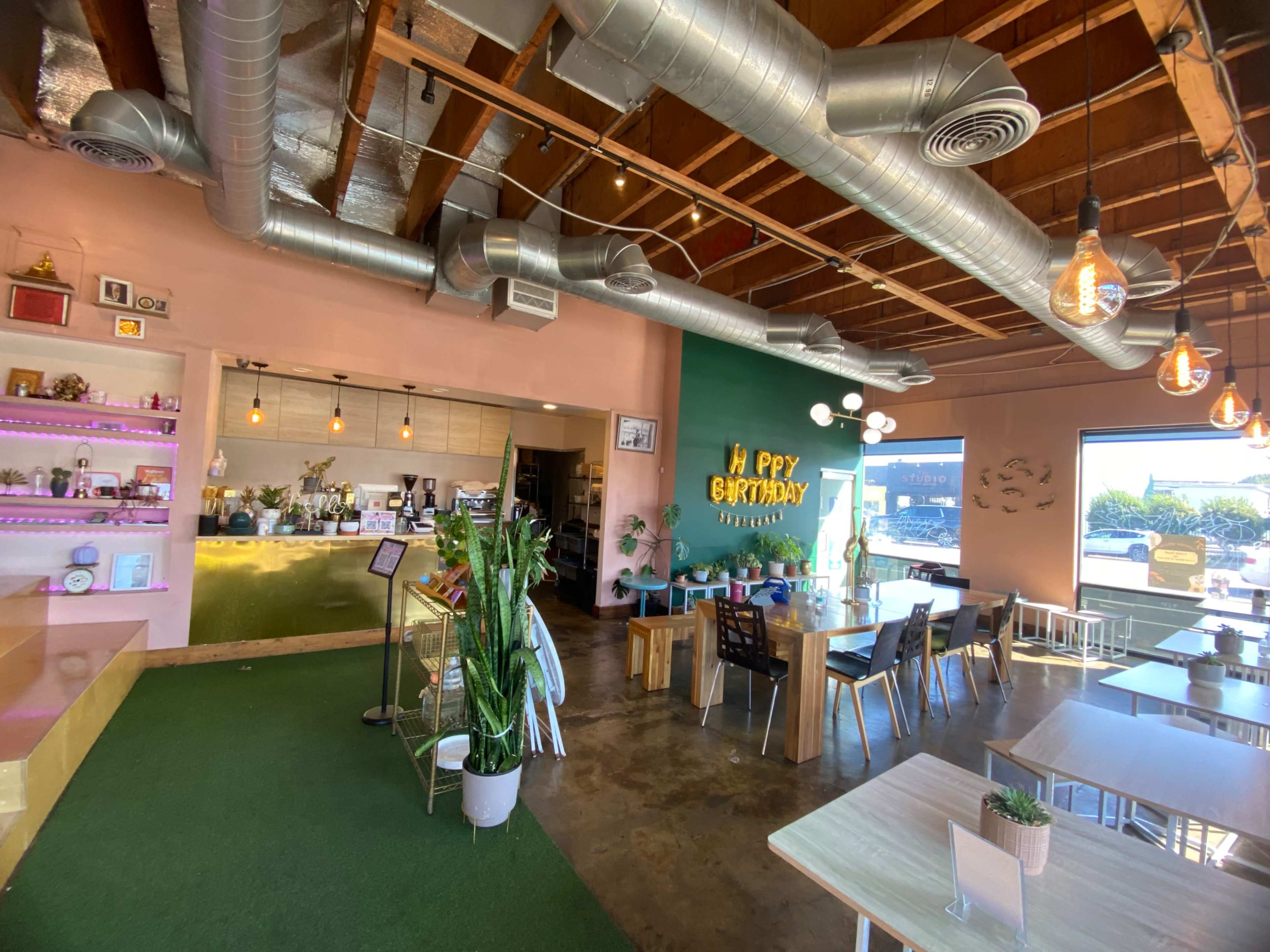 A bright and modern café interior with a green accent wall, birthday decorations, and both seating and a service counter.