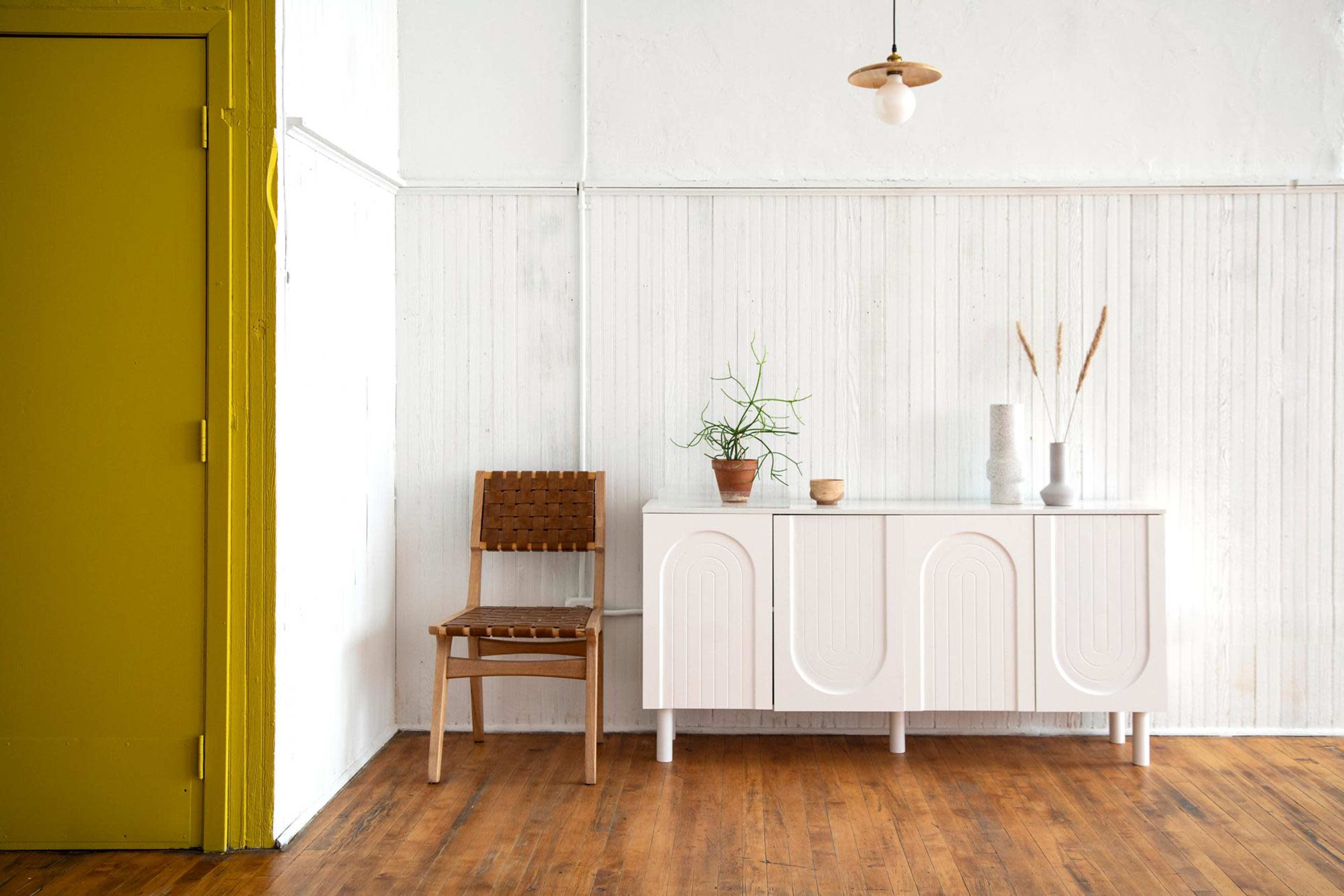 A simple room features a white cabinet and a wooden chair next to a green door against a light-colored wall.