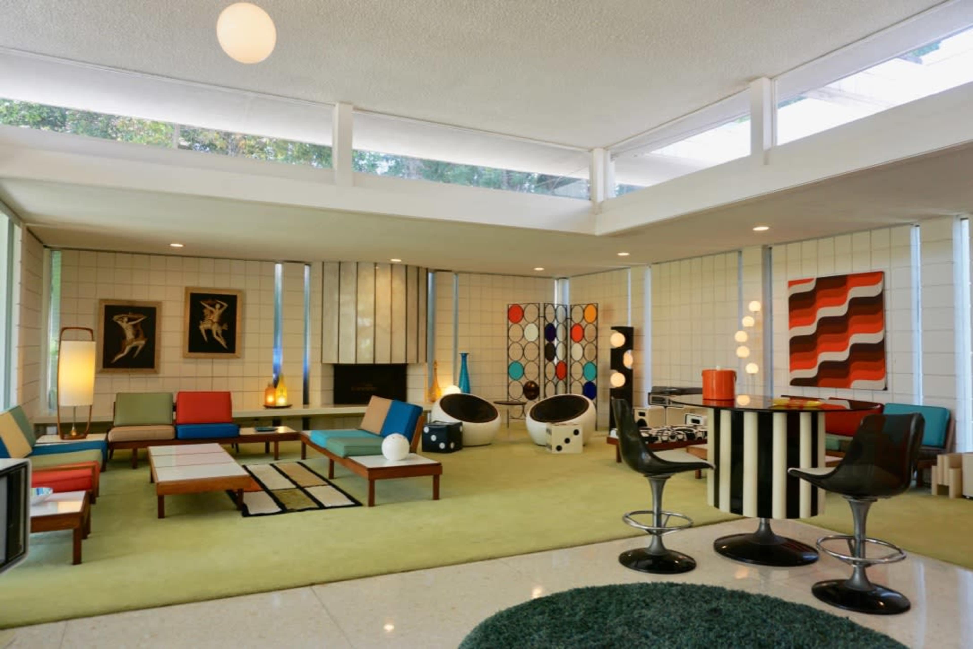 A mid-century modern living room featuring colorful furniture, geometric wall art, and large windows that bring in natural light.