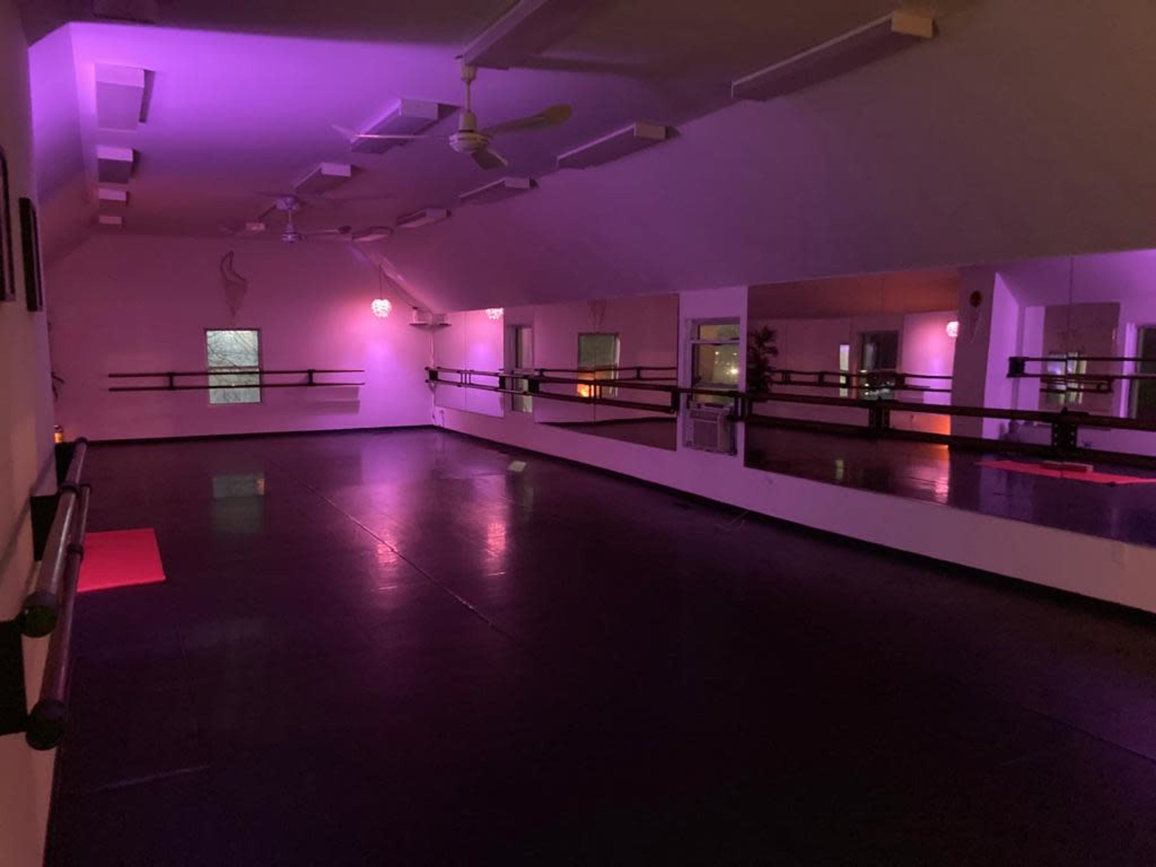 An empty dance studio with purple lighting and large mirrors along one wall.