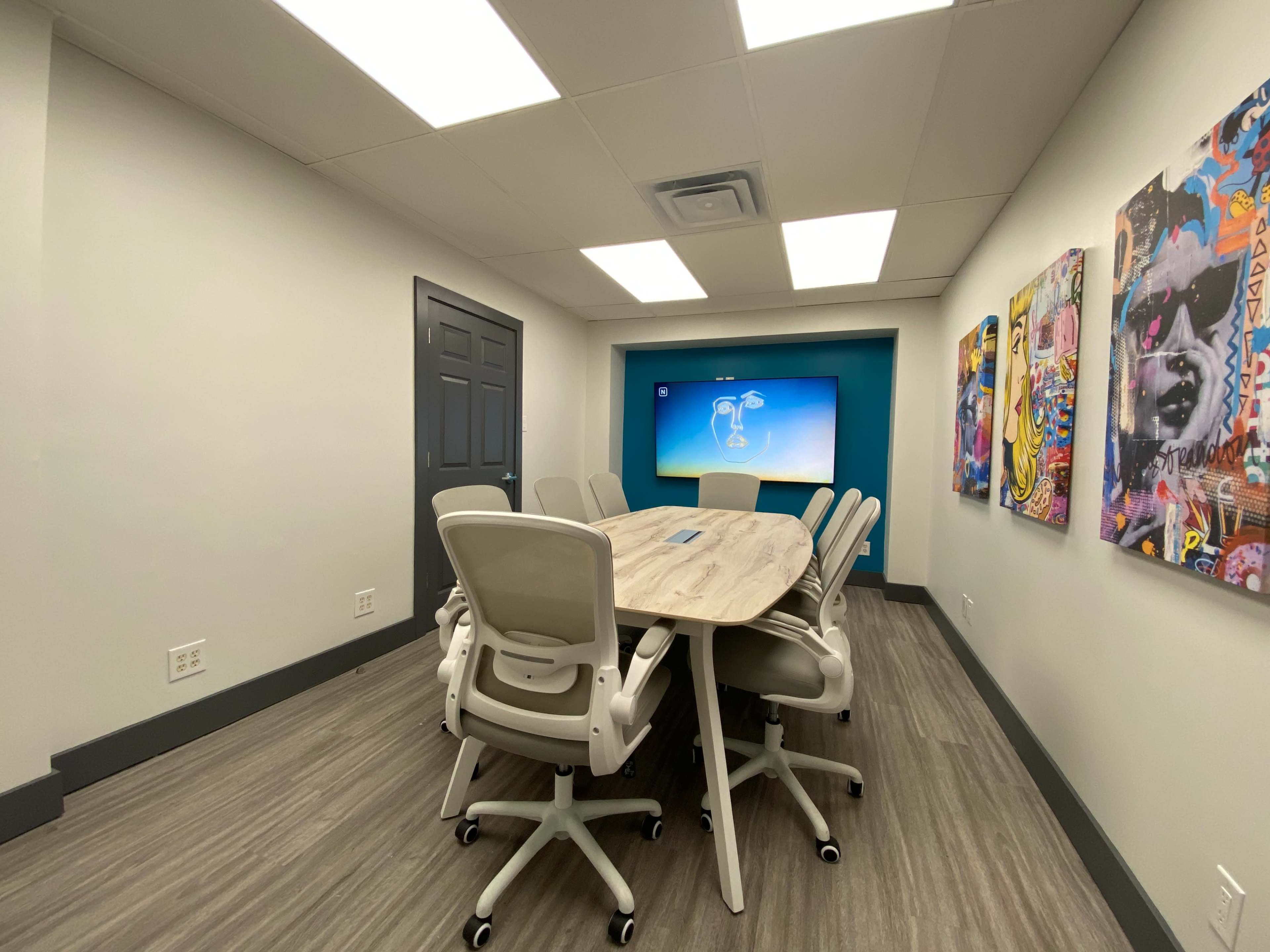 A modern conference room with a large table surrounded by white chairs and a wall-mounted screen displaying a colorful presentation.