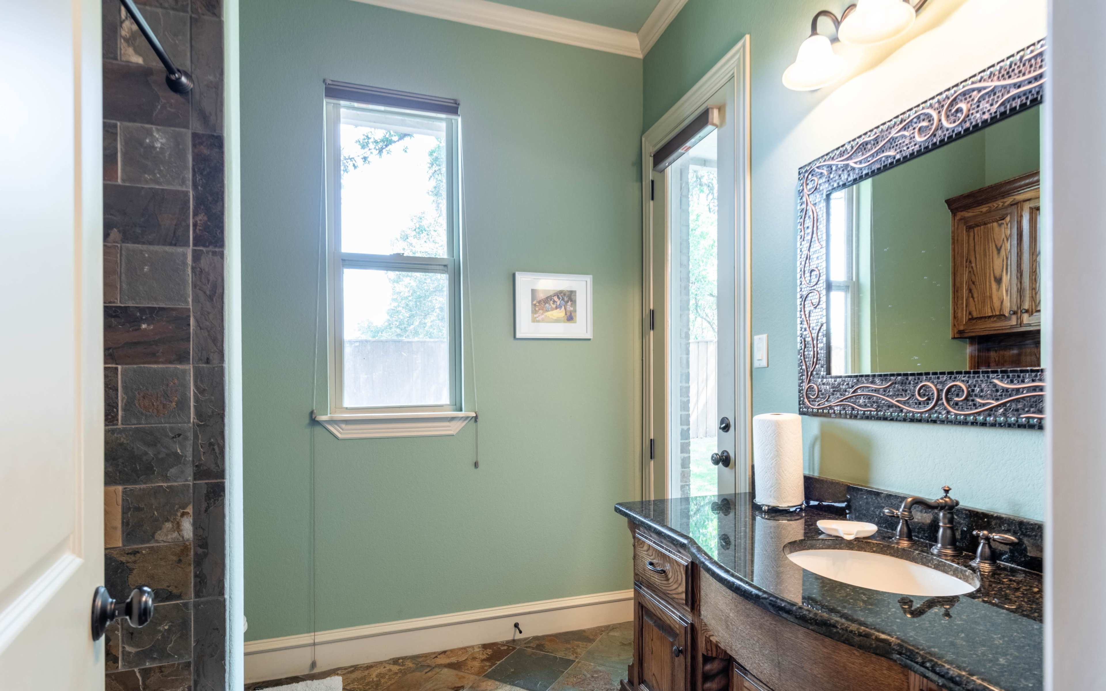 A well-lit bathroom featuring a granite countertop vanity, a large mirror, and light green walls.