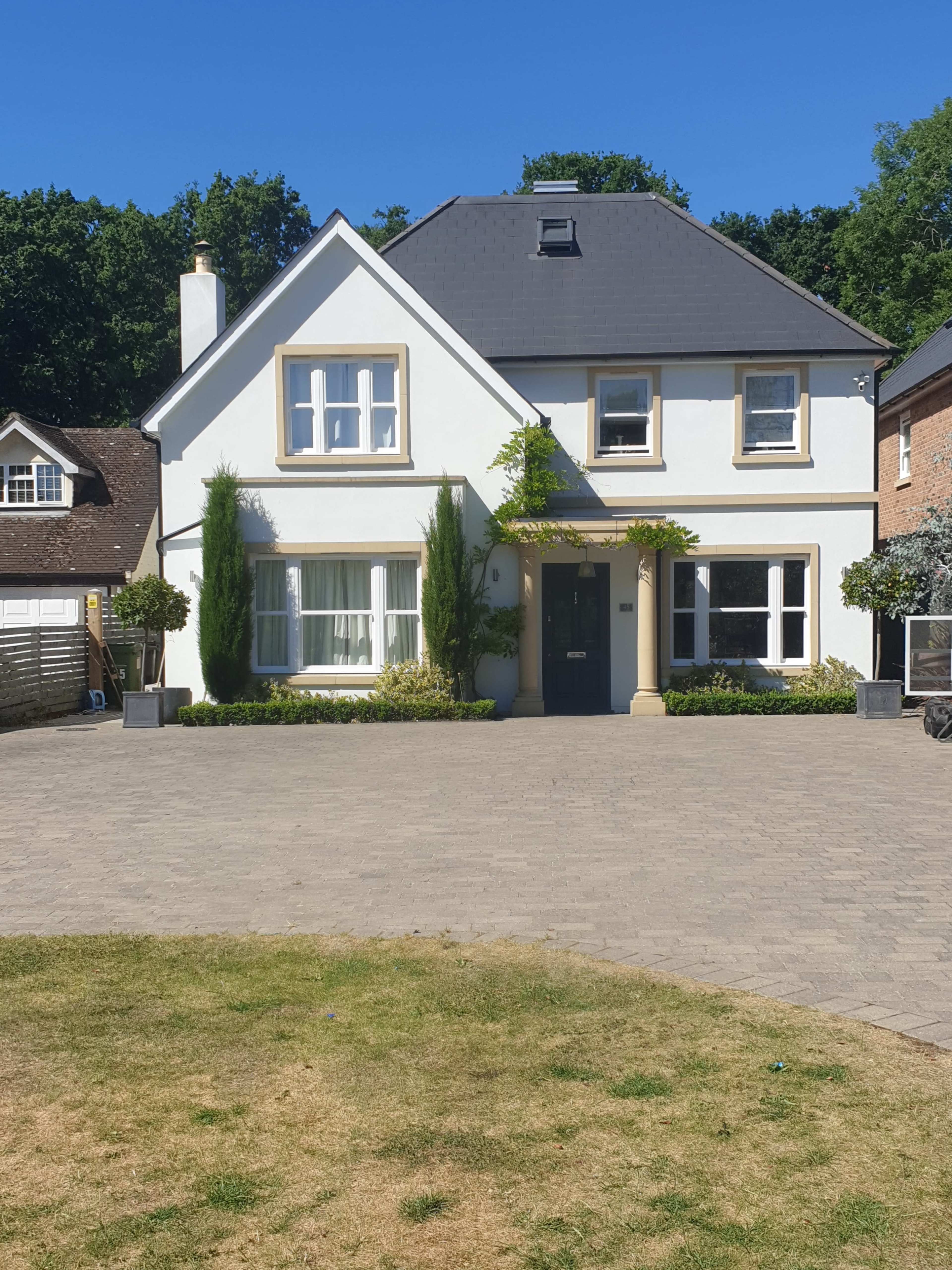 A two-story white house with a gray roof and a landscaped front yard, situated on a paved driveway.